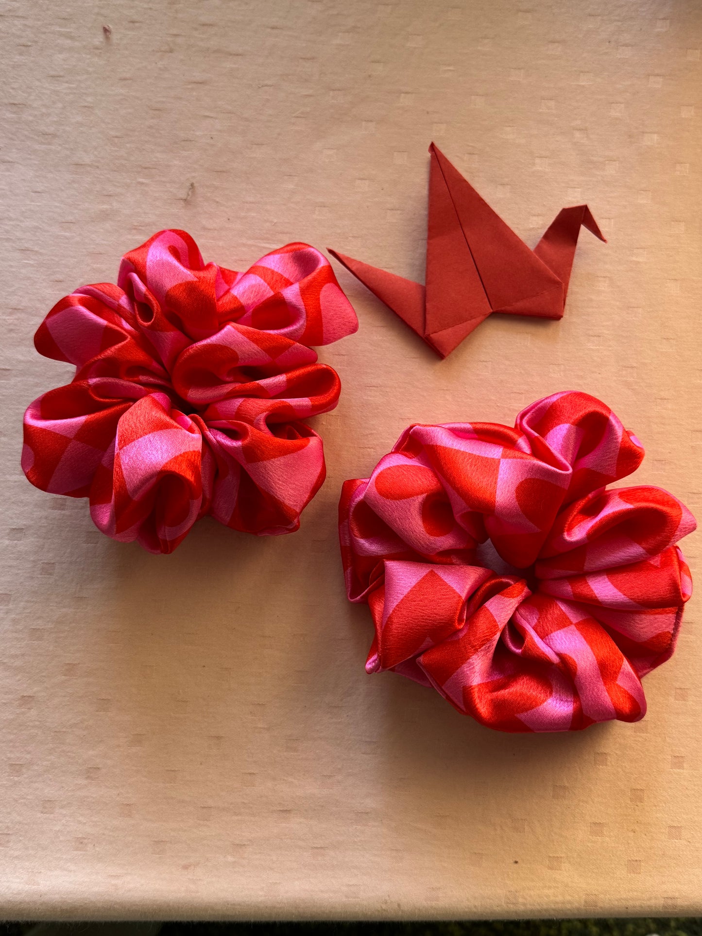 Two XL satin scrunchies in pink with cute heart patterns, designed for all hair types (thick, thin, or voluminous) as a gentle yet secure hair tie or trendy wrist accessory.