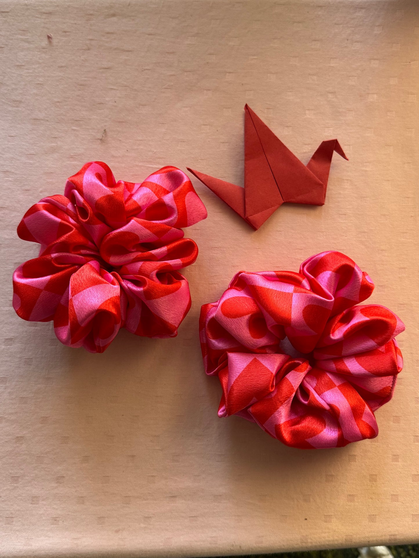 Two XL satin scrunchies in pink with cute heart patterns, designed for all hair types (thick, thin, or voluminous) as a gentle yet secure hair tie or trendy wrist accessory.