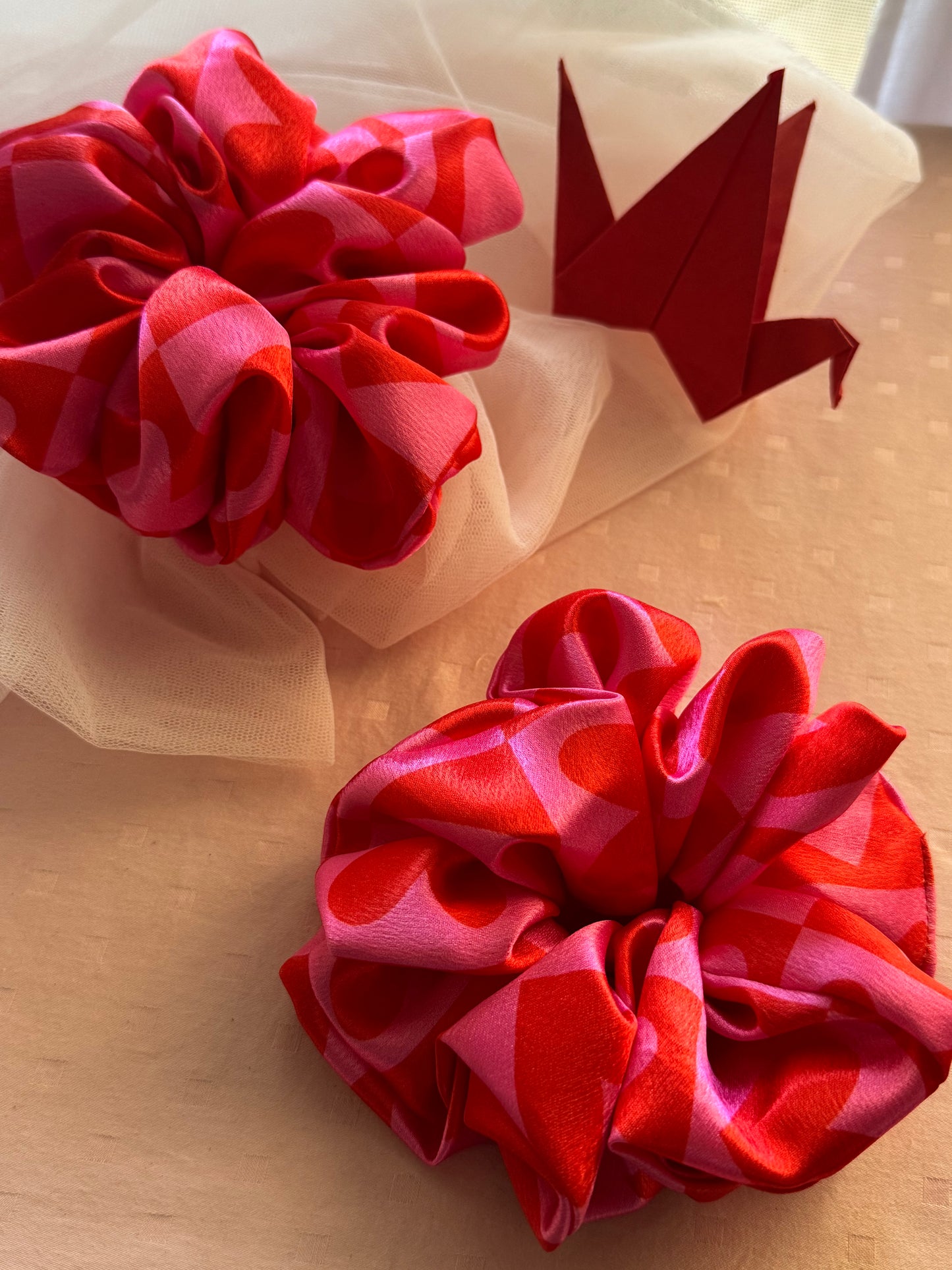 Two XL satin scrunchies in pink with cute heart patterns, designed for all hair types (thick, thin, or voluminous) as a gentle yet secure hair tie or trendy wrist accessory.