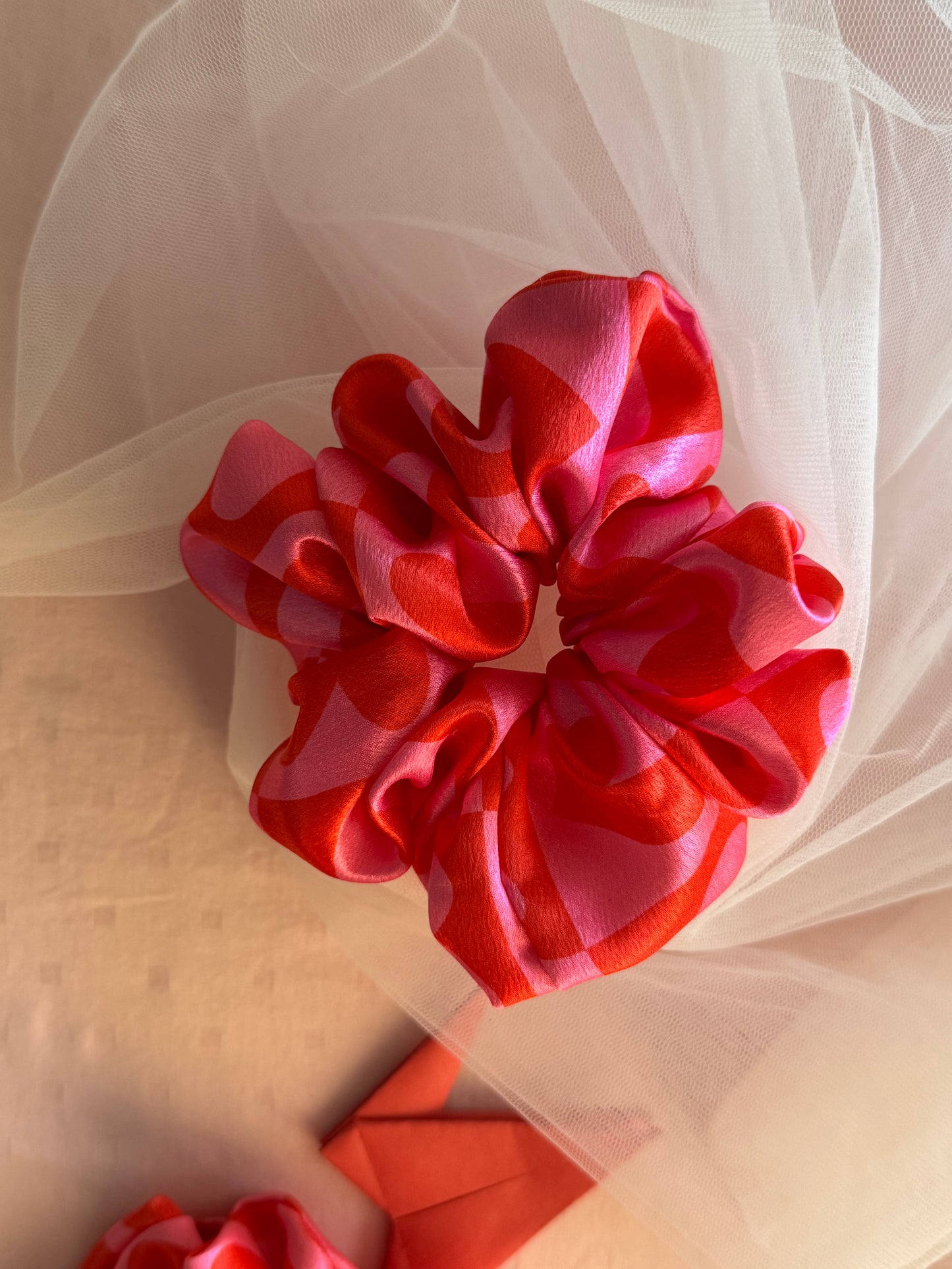 A charming pink satin scrunchie with a playful heart print, made from soft printed satin fabric to prevent hair damage—perfect for ponytails, buns, and stylish everyday hair accessories
