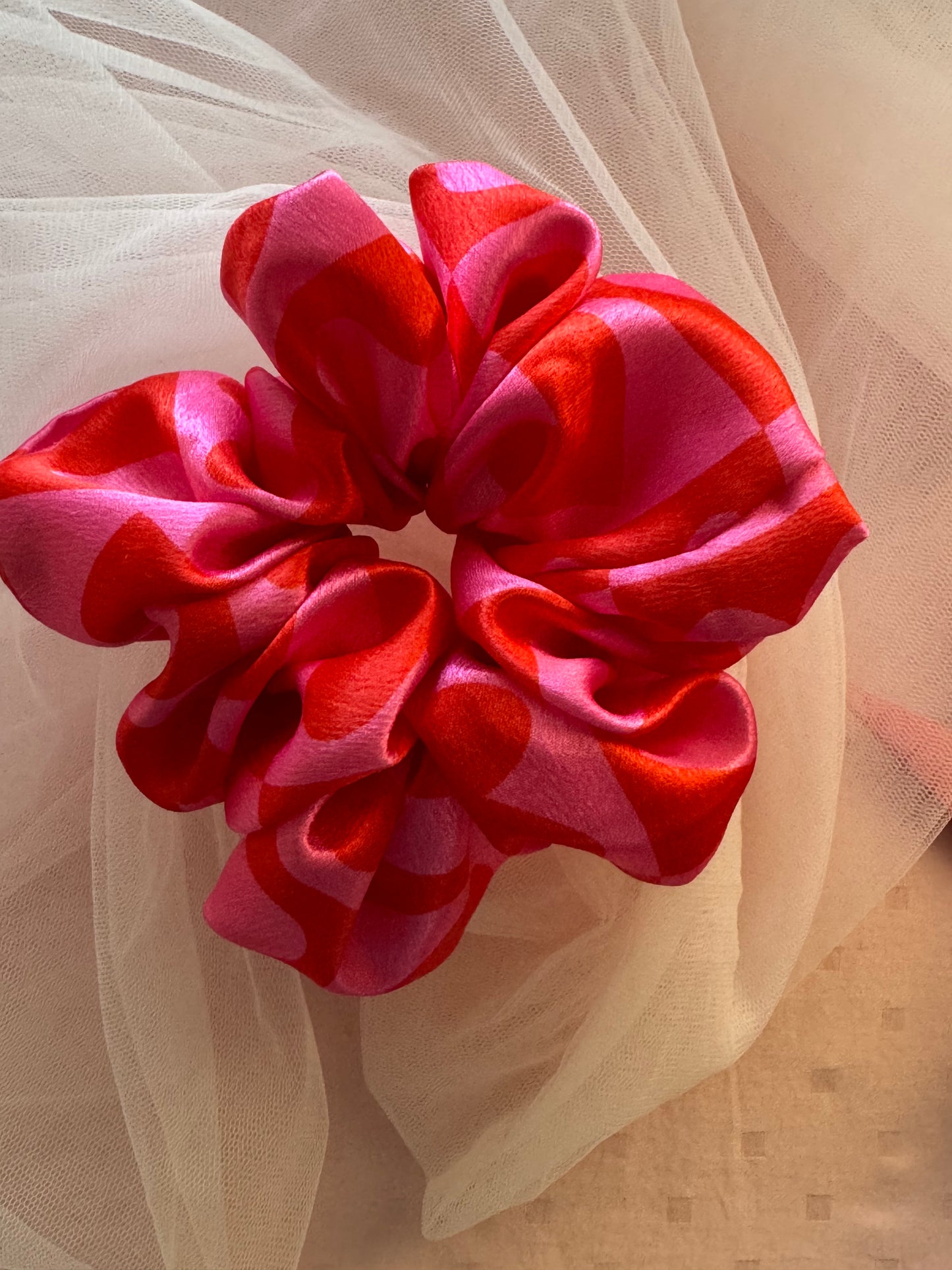 A charming pink satin scrunchie with a playful heart print, made from soft printed satin fabric to prevent hair damage—perfect for ponytails, buns, and stylish everyday hair accessories