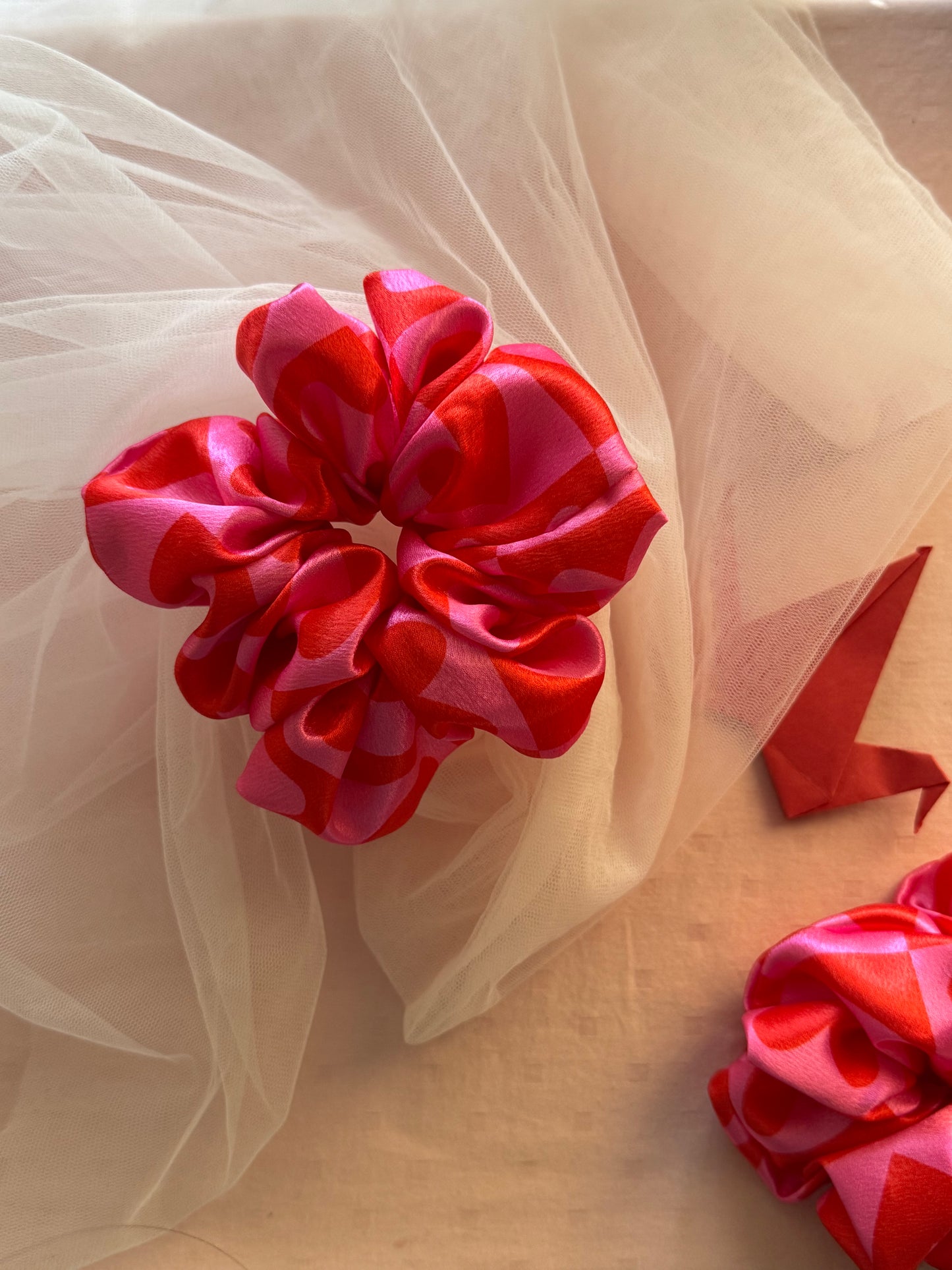 A charming pink satin scrunchie with a playful heart print, made from soft printed satin fabric to prevent hair damage—perfect for ponytails, buns, and stylish everyday hair accessories