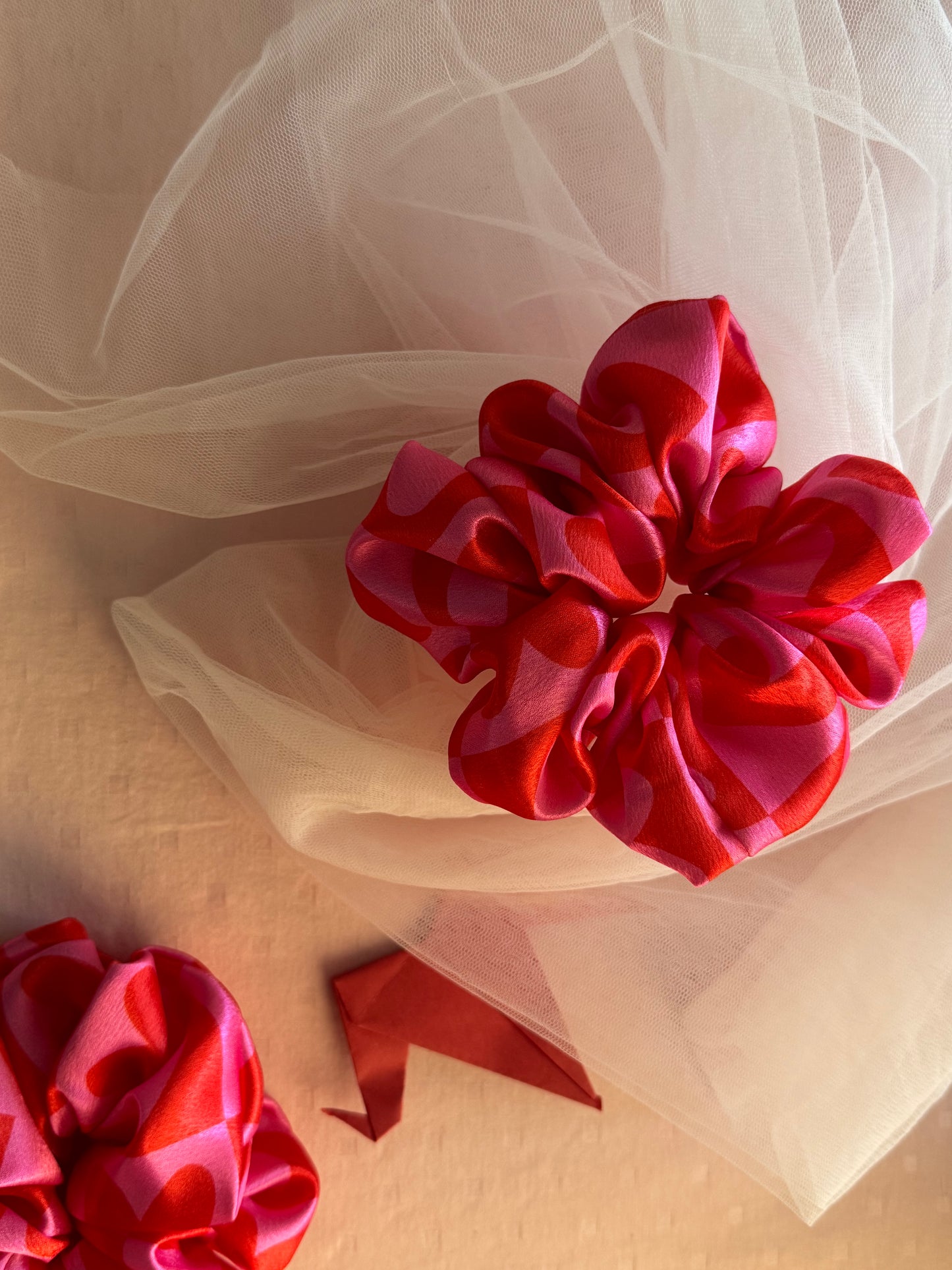 A charming pink satin scrunchie with a playful heart print, made from soft printed satin fabric to prevent hair damage—perfect for ponytails, buns, and stylish everyday hair accessories
