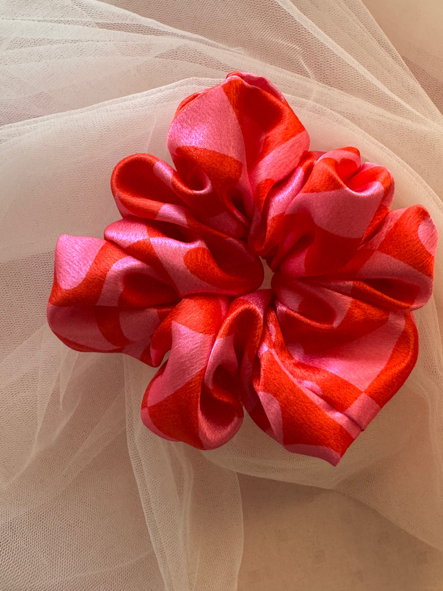 A charming pink satin scrunchie with a playful heart print, made from soft printed satin fabric to prevent hair damage—perfect for ponytails, buns, and stylish everyday hair accessories