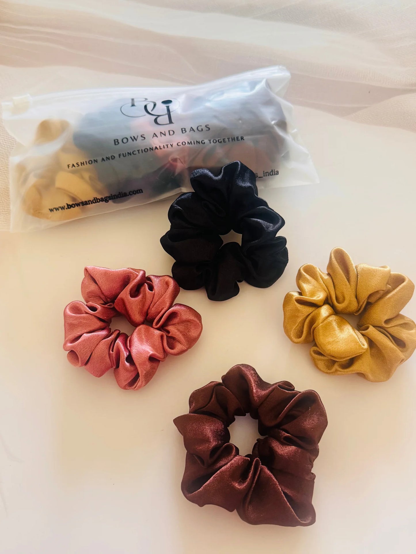 Pack of 4 satin scrunchies in black, gold, rust, and burgundy by Bows and Bags India handmade hair accessories displayed flat