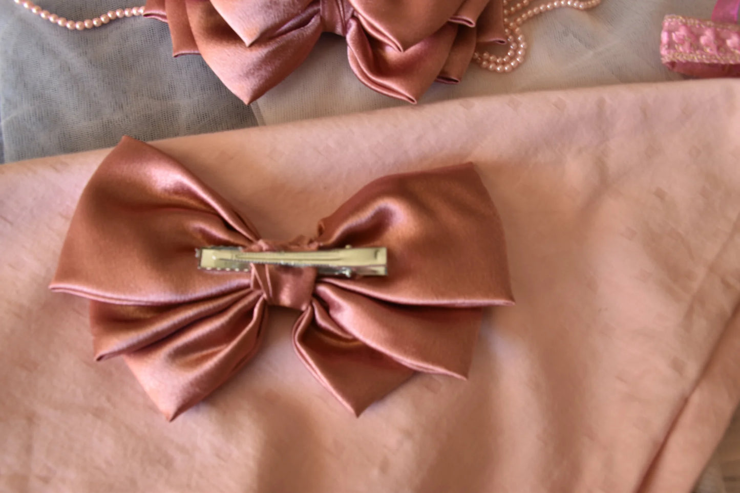 Metallic peach satin hair bow by Bows and Bags India displayed on wrist showing glossy texture and elegant drape of handmade
