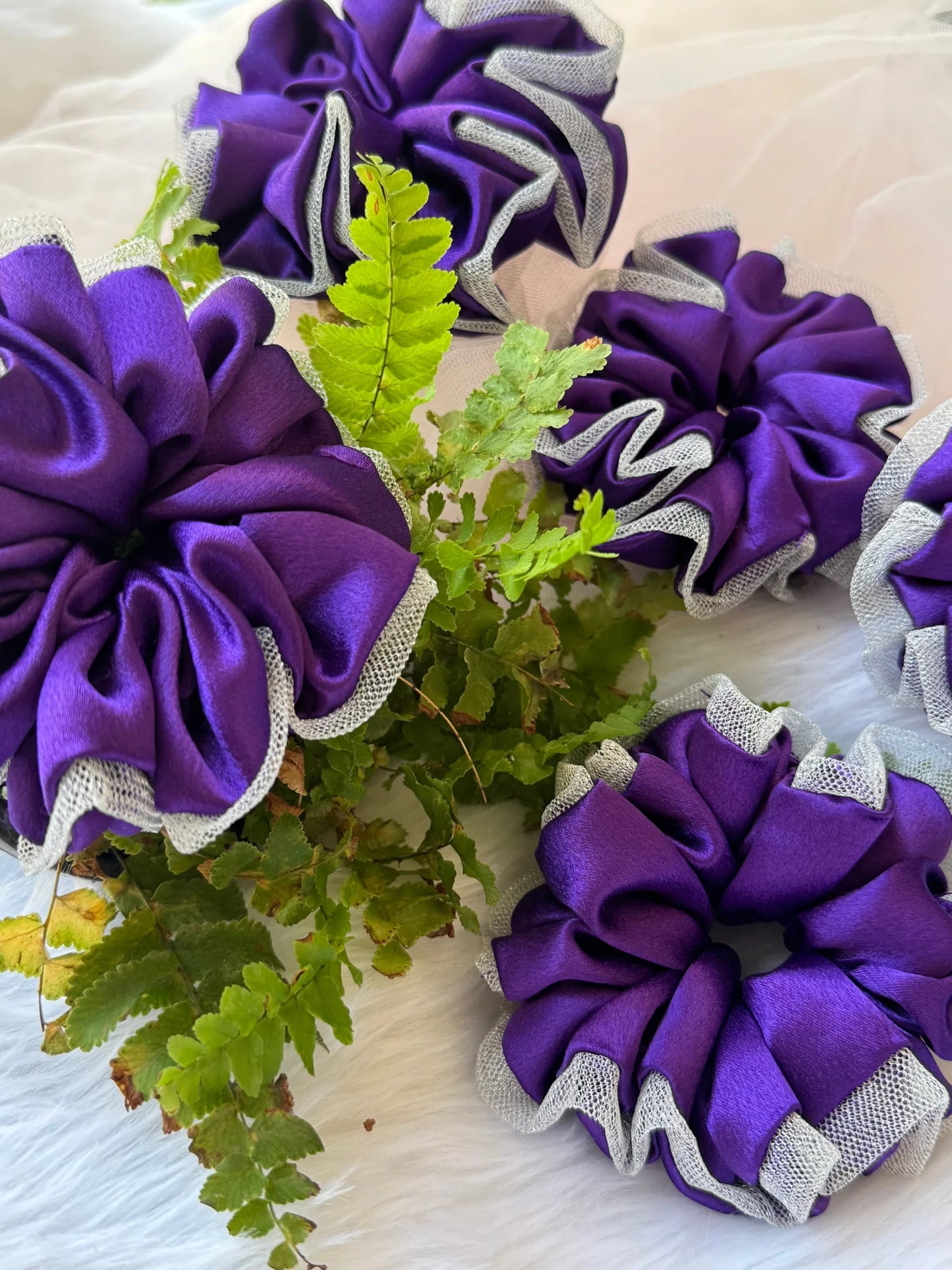 Purple satin scrunchie with silver net border, handmade hair accessory by Bows and Bags India, displayed with green foliage