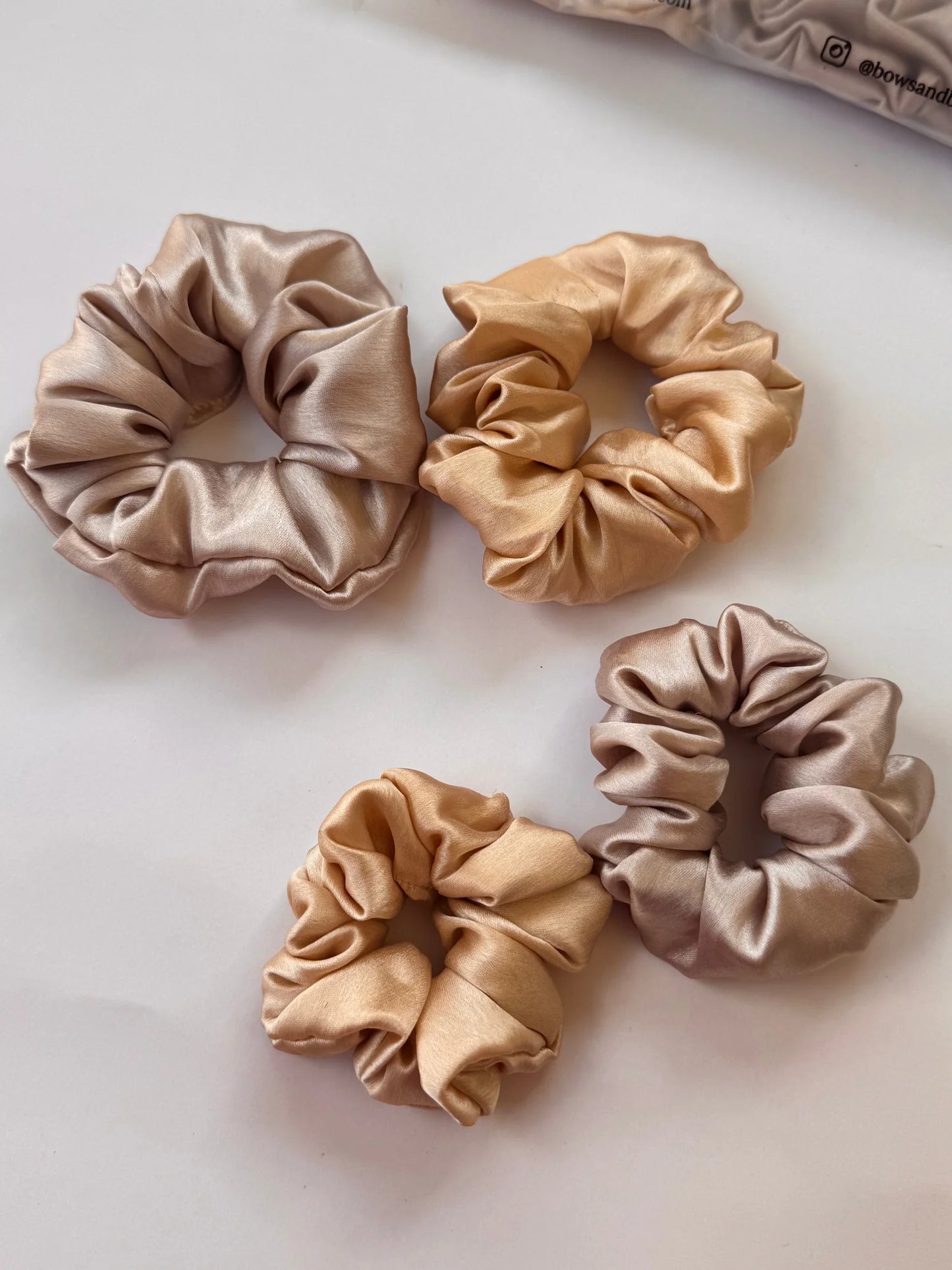 Flat lay of four premium satin scrunchies in gold and champagne silver tones, mini and large sizes by Bows and Bags India
