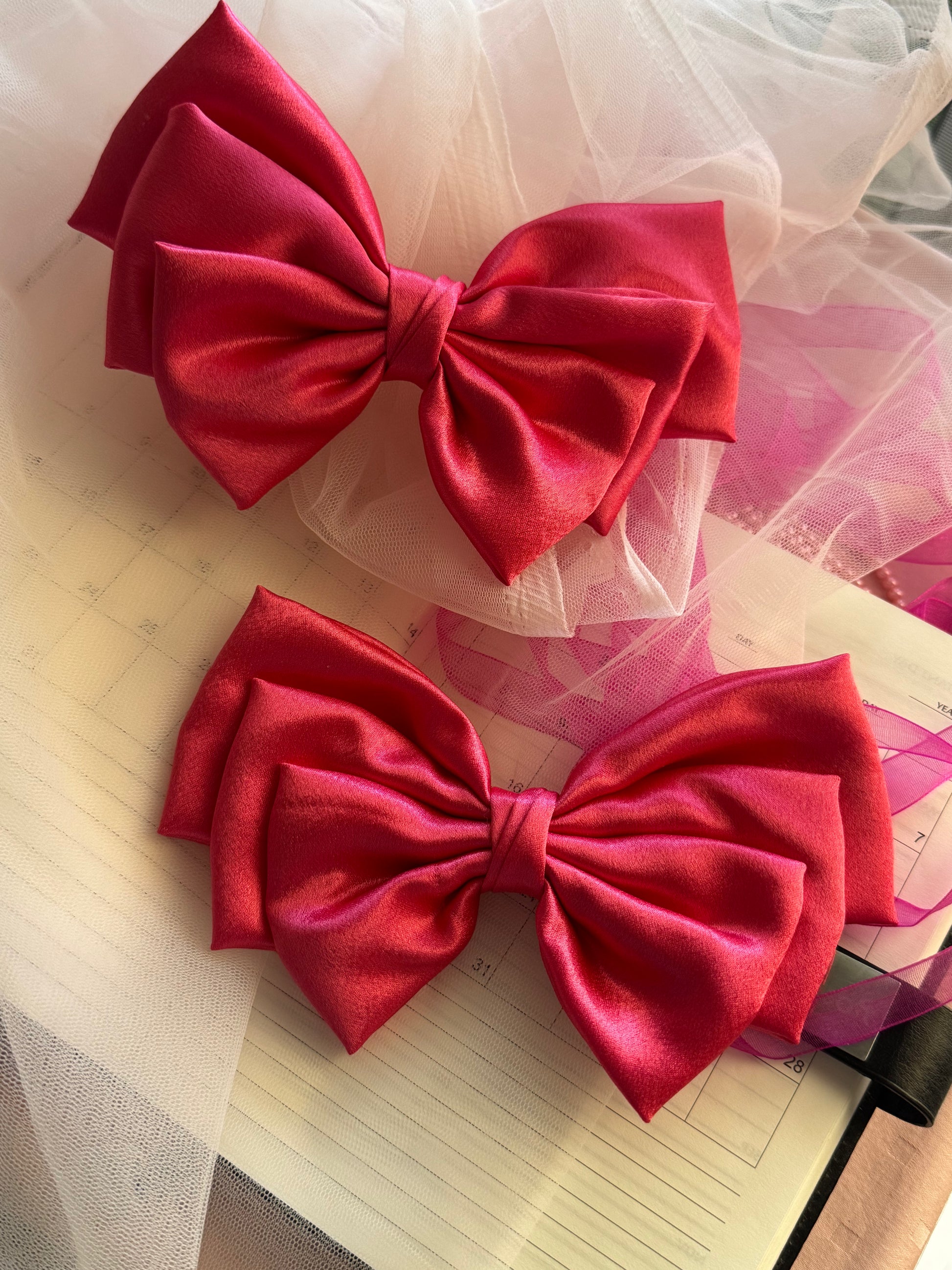 Two Satin Hair bows with Clip Front Size, beautiful glossy Pink Color with light and dark, with Props kept ]almost parallely in reverse order.

