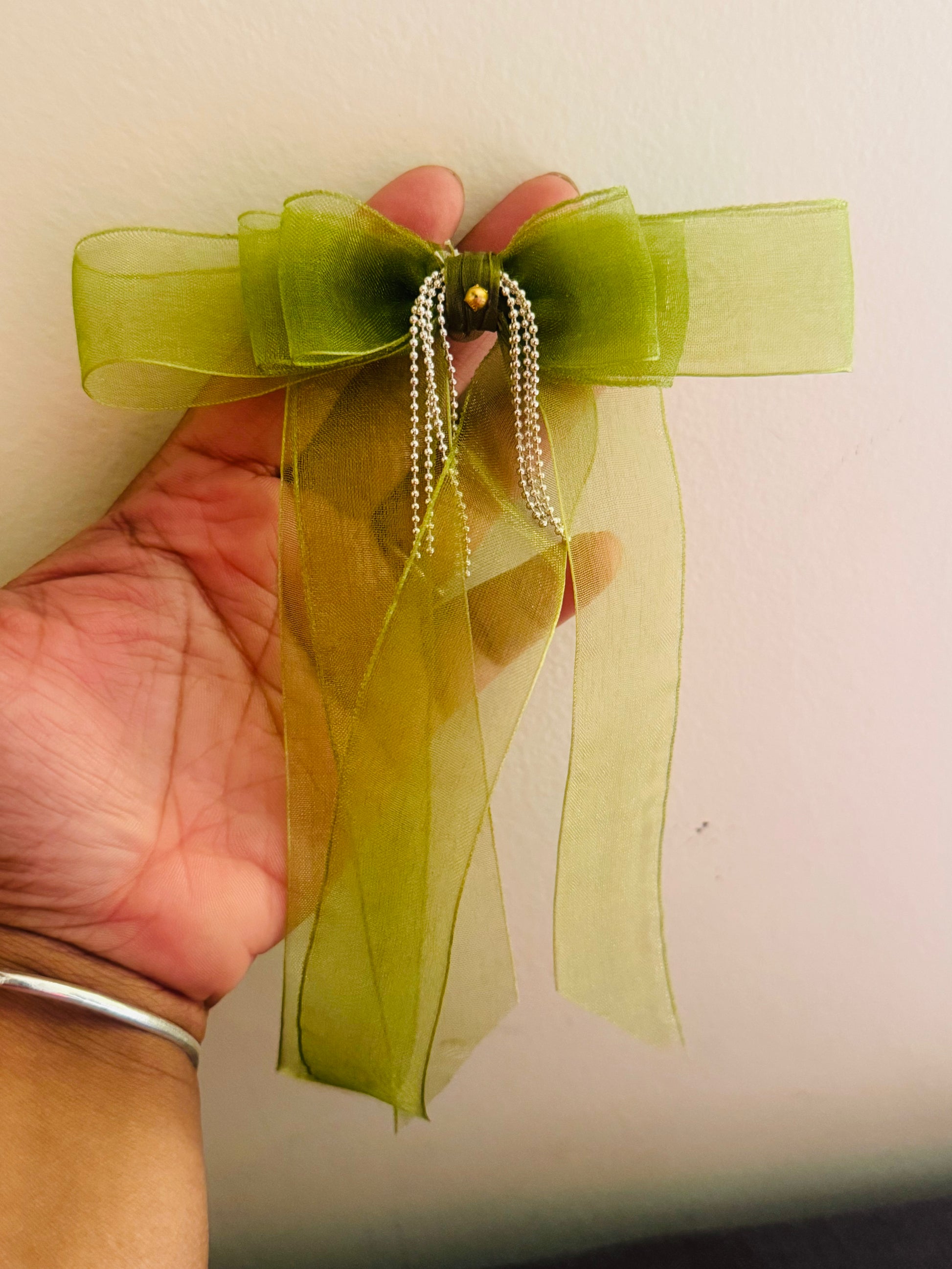 Tinker Bell Hair Bow Clip - Front view of a light green organza hair bow with a delicate silver chain detail for a graceful and elegant look held in a hand for comparison.