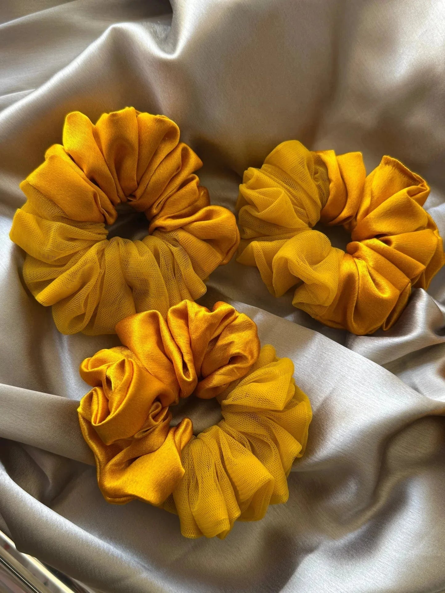 Three mustard yellow handmade scrunchies with net detailing by Bows and Bags India on cream fabric, showing texture and