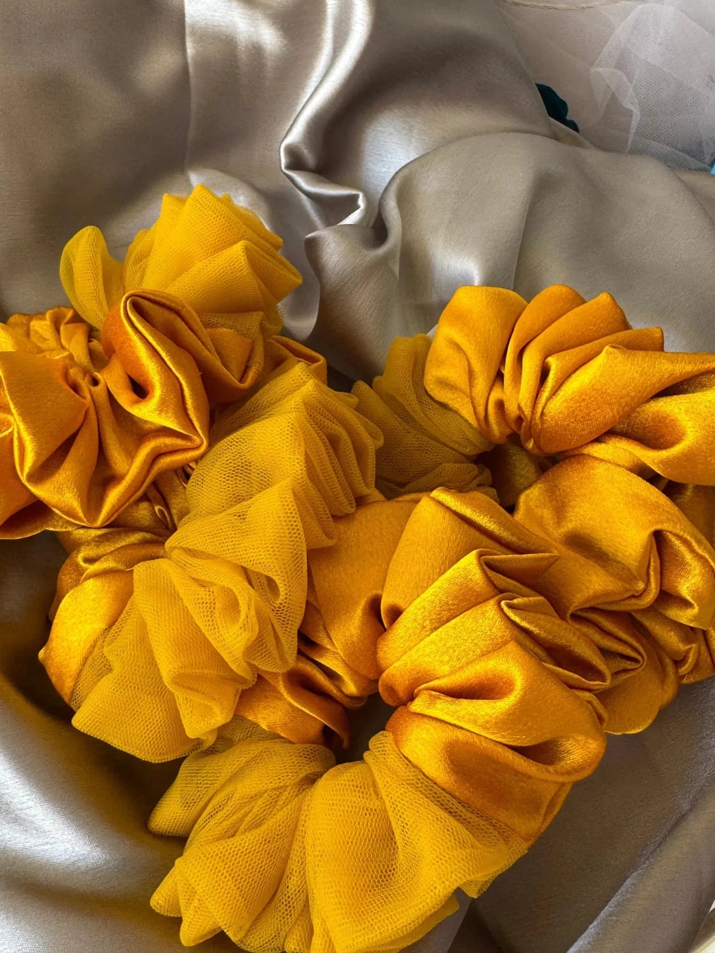 Mustard yellow satin and net scrunchies arranged on cream fabric by Bows and Bags India, showcasing handmade hair