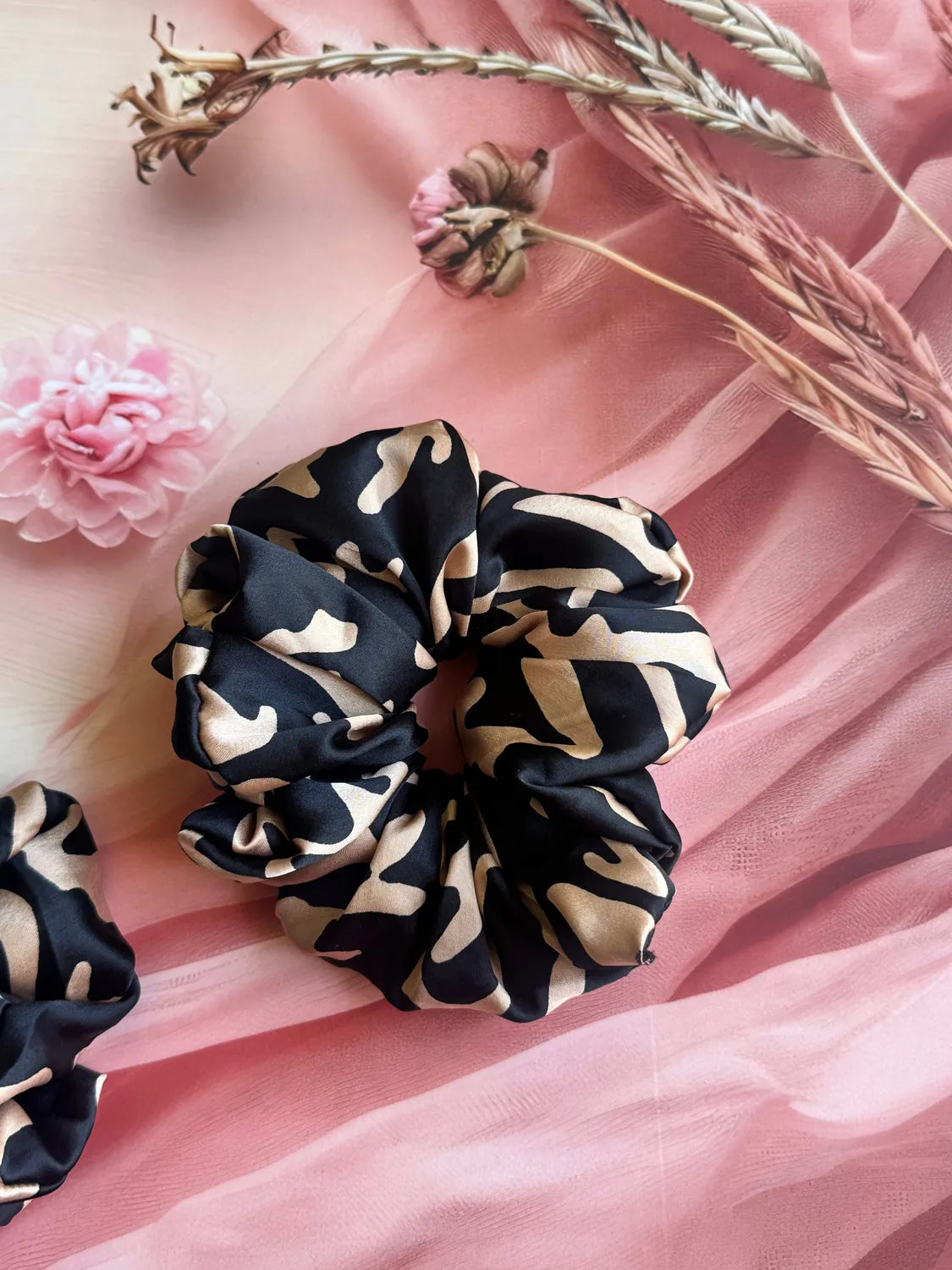Black Savanna abstract animal print satin scrunchie by Bows and Bags India displayed on pink fabric with dried flowers