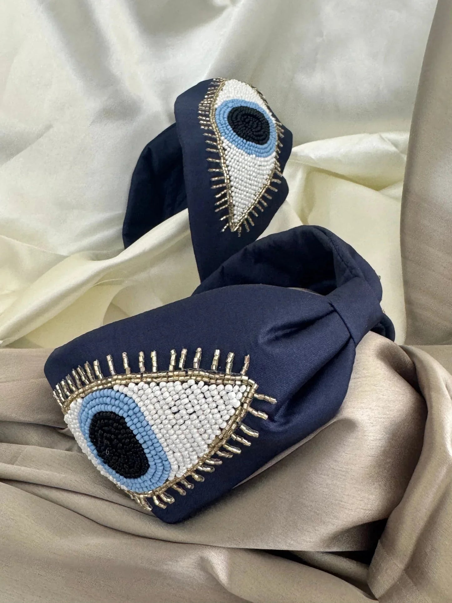Navy blue satin handmade beaded headband with evil eye design by Bows and Bags India, lifestyle shot on cream fabric