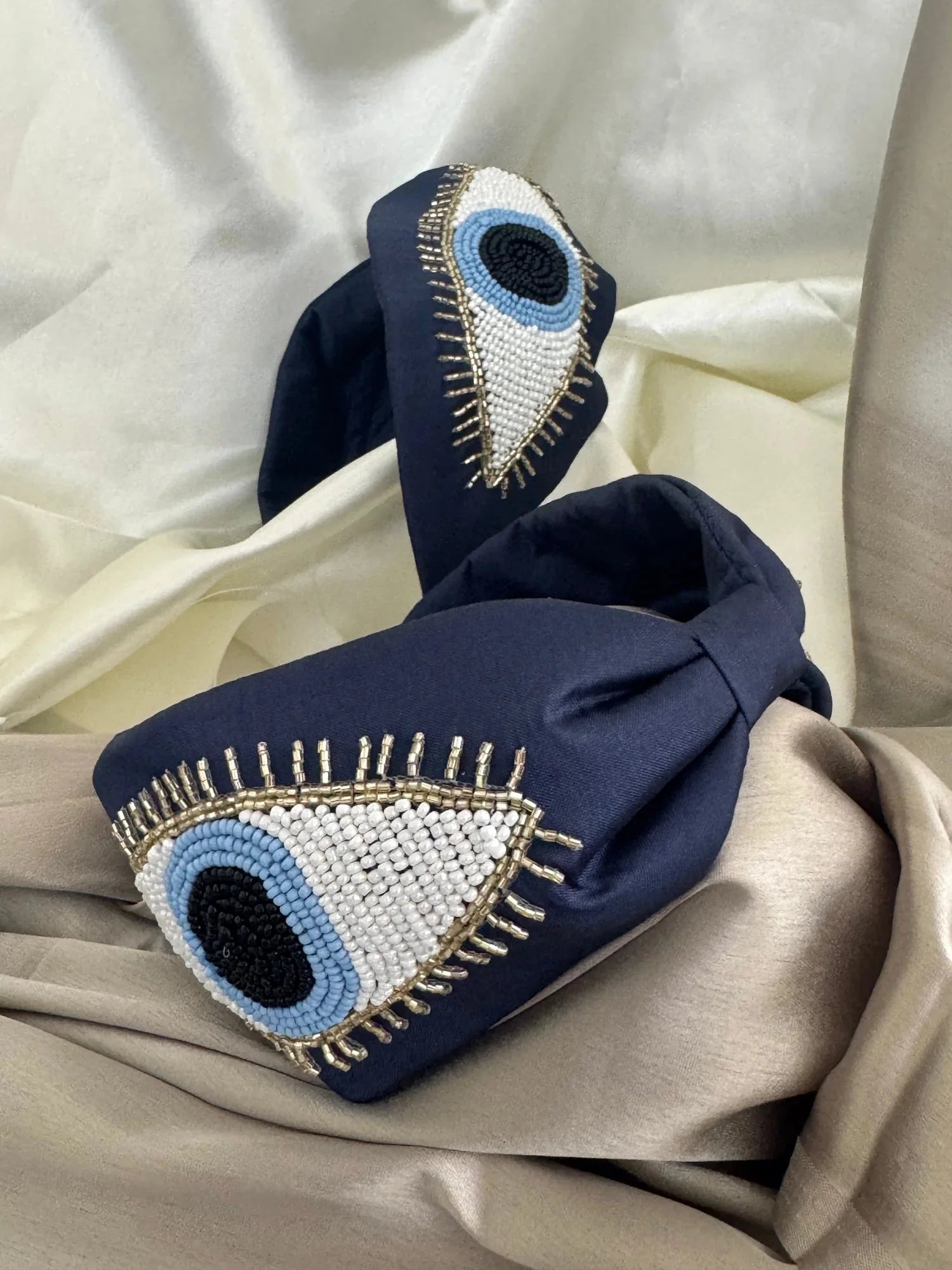 Navy blue satin handmade beaded headband with evil eye design by Bows and Bags India, lifestyle shot on cream fabric