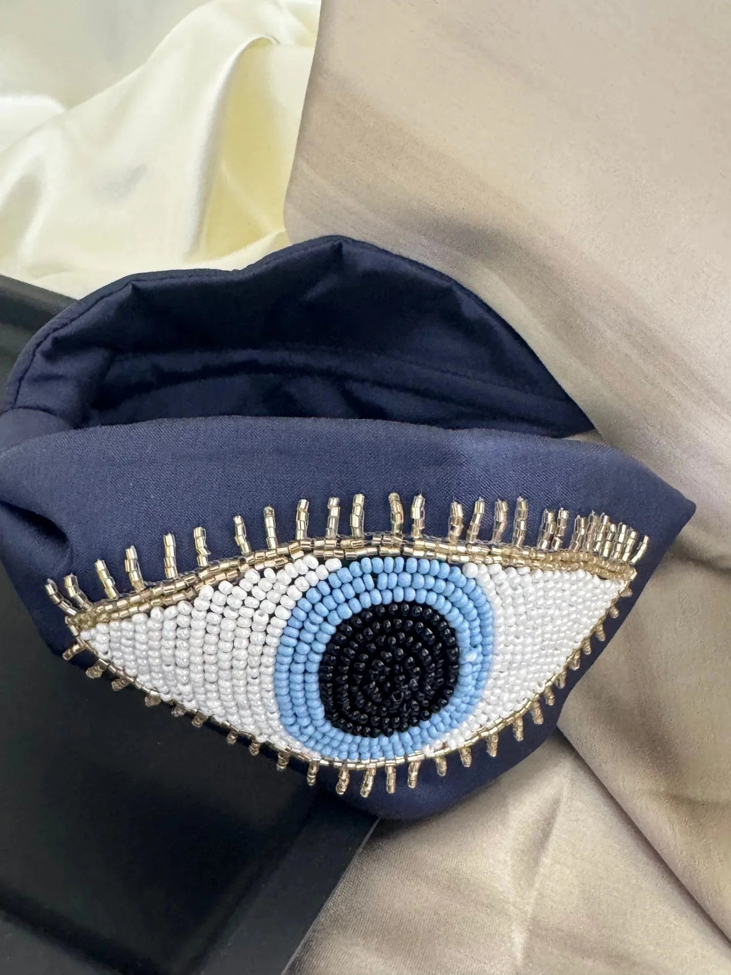 Close-up detail of navy blue satin handmade beaded headband with intricate evil eye design featuring white and light blue