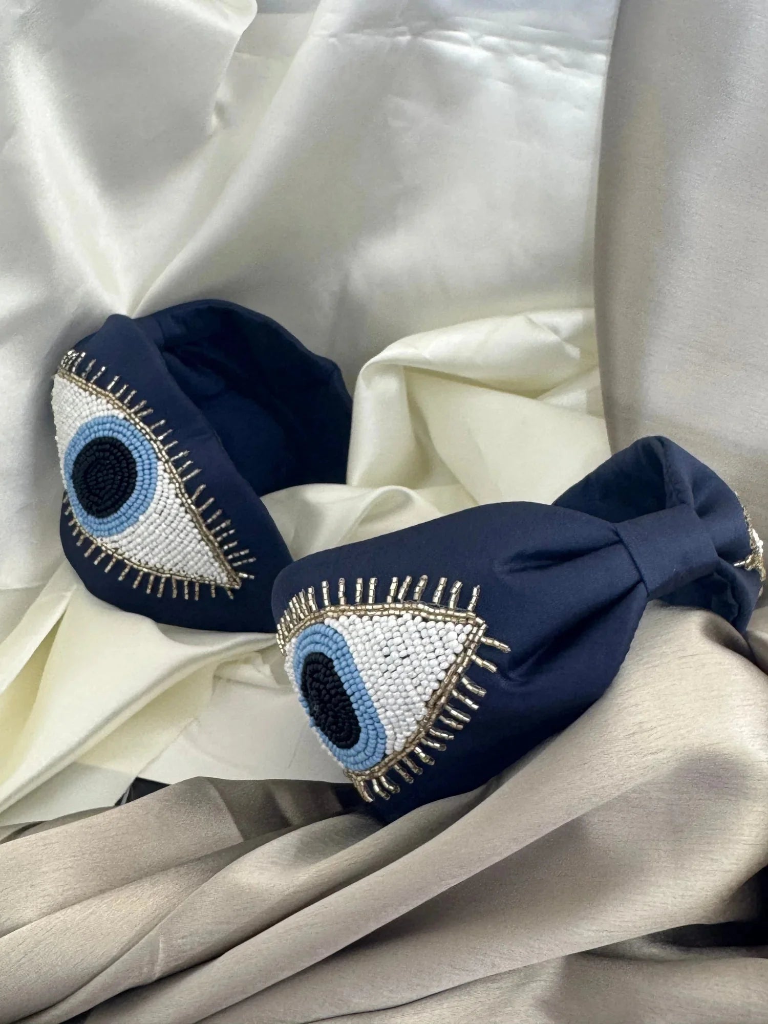 Navy blue satin handmade headband with beaded evil eye design by Bows and Bags India, detailed close-up on cream fabric