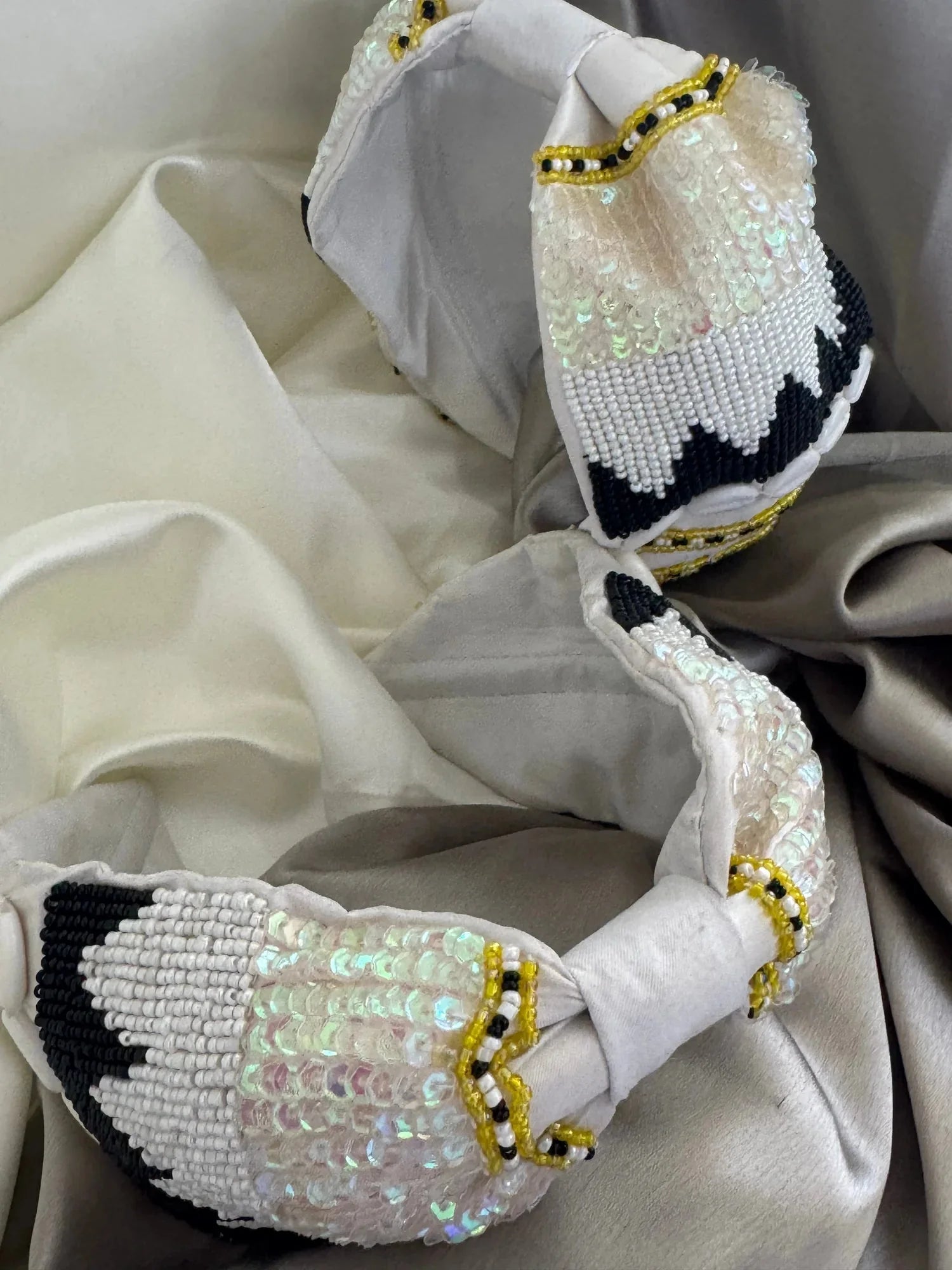 Boho Bling white satin handmade headband with iridescent sequins and black beaded detailing, flat lay on cream fabric by