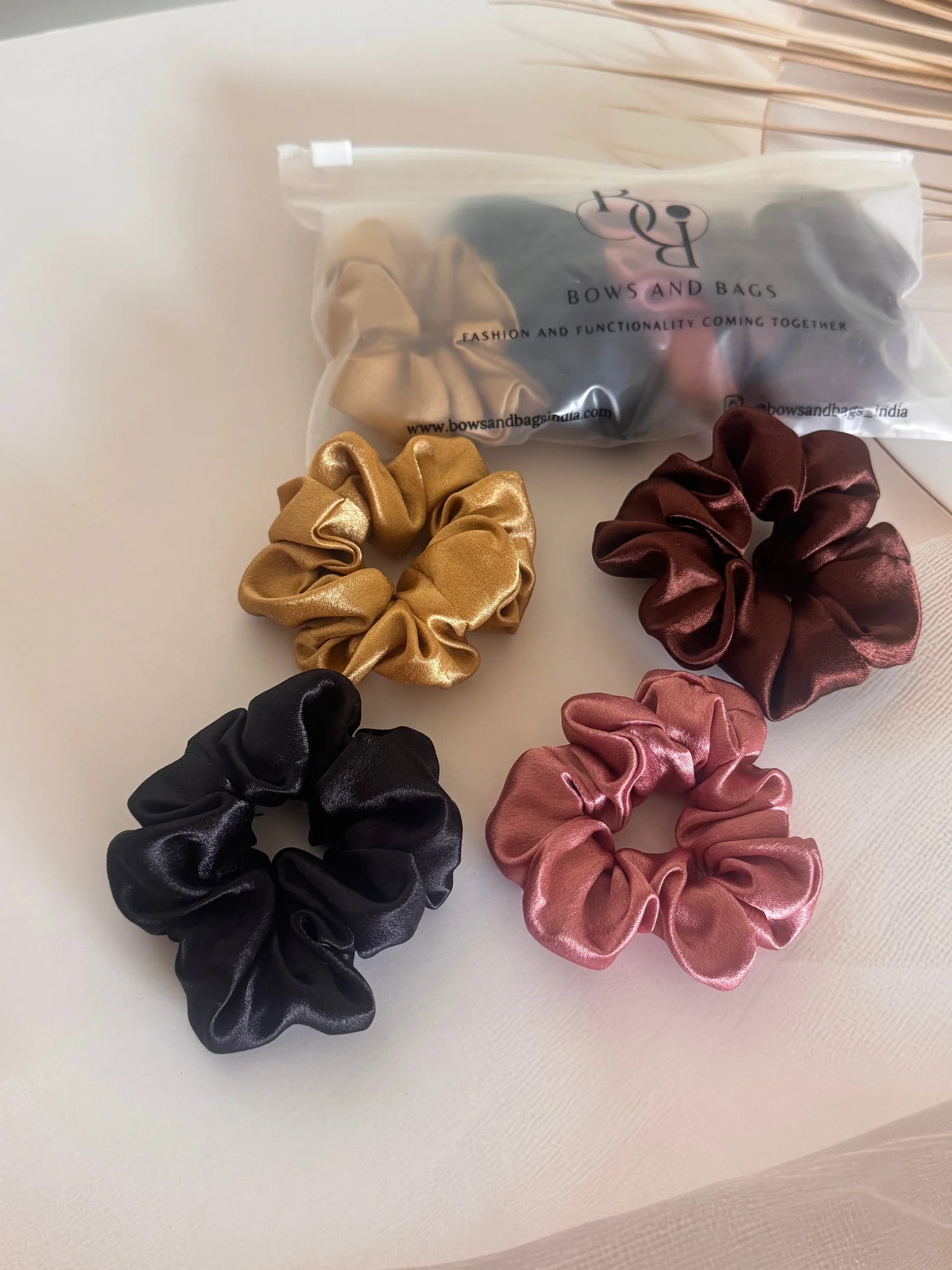 Four premium satin scrunchies in black, gold, rust, and burgundy by Bows and Bags India displayed on white surface, handmade
