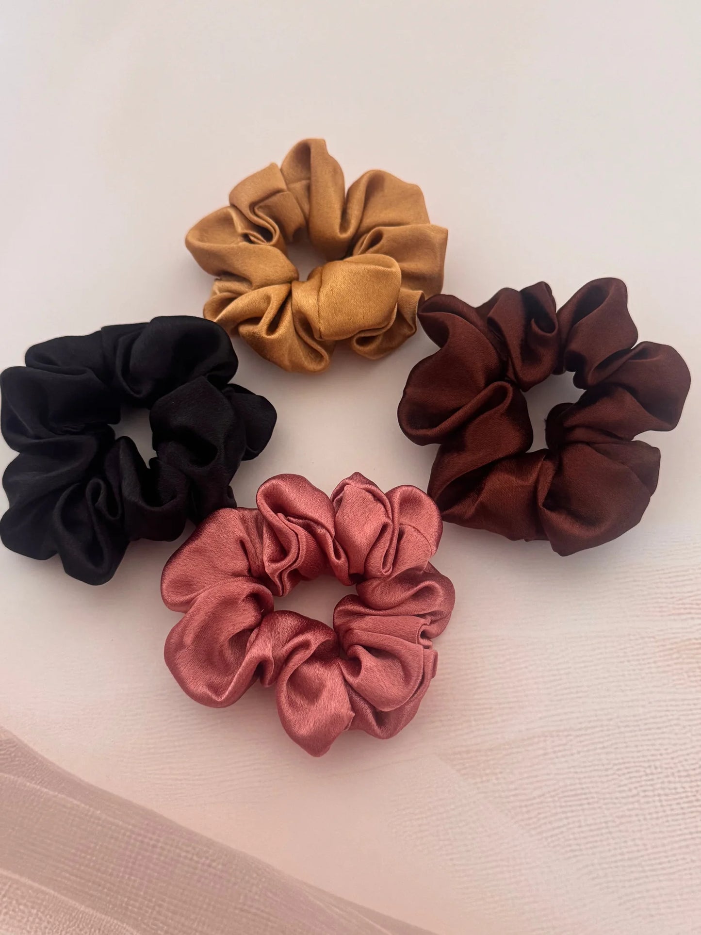 Four satin scrunchies in black, gold, rust, and burgundy by Bows and Bags India handmade hair accessories, arranged on white