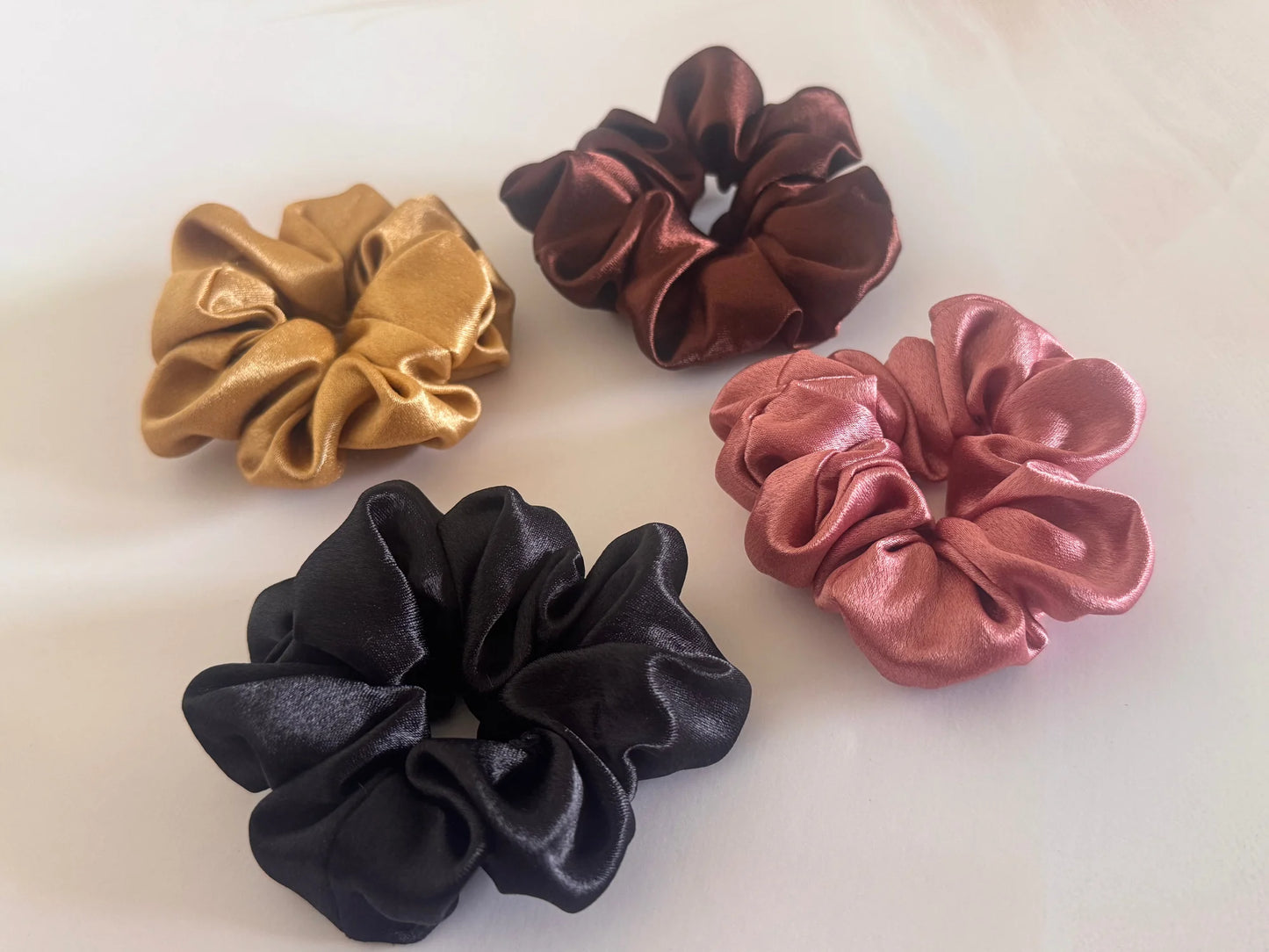 Four premium satin scrunchies in black, gold, rust, and burgundy by Bows and Bags India displayed on white surface showing