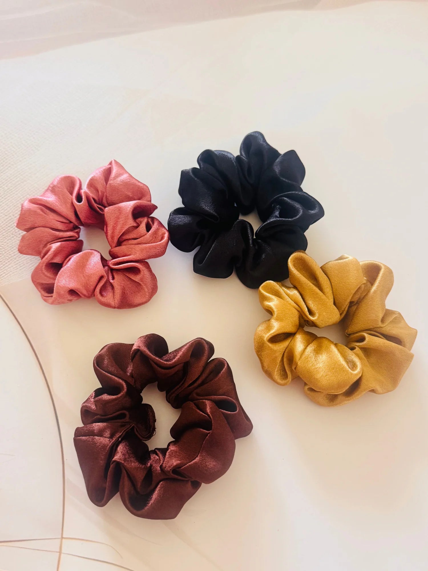 Four premium satin scrunchies by Bows and Bags India in black, burgundy, rust, and gold displayed on white surface