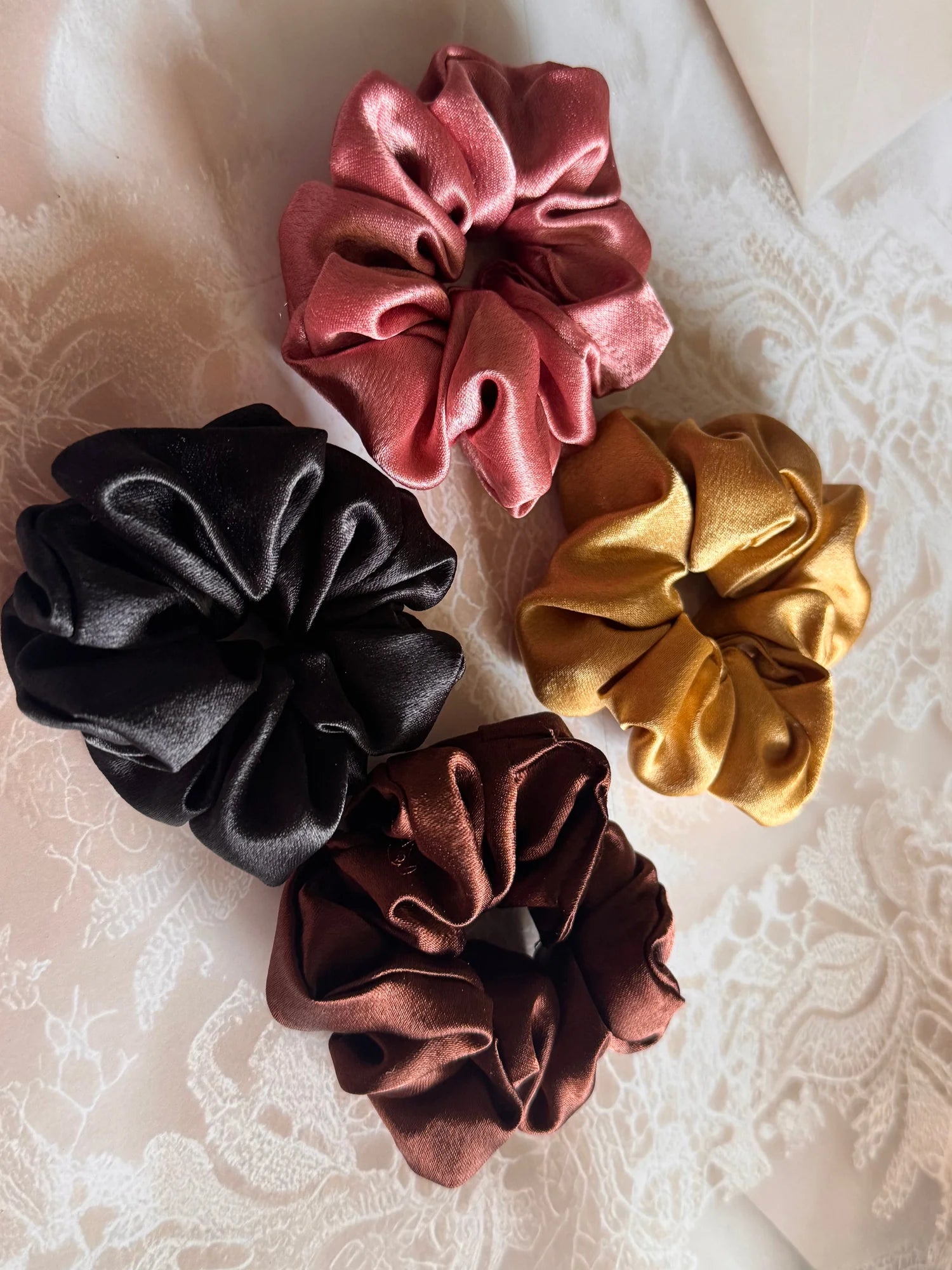 Four premium satin scrunchies in black, gold, rust, and burgundy by Bows and Bags India handmade hair accessories flat lay