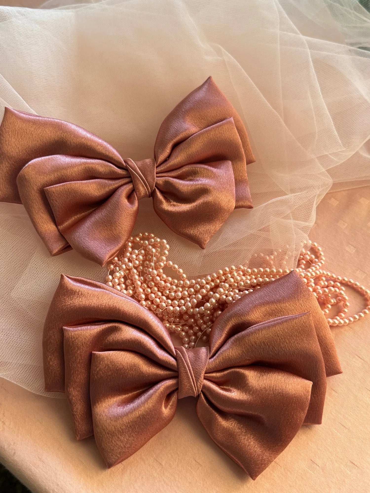 Metallic peach satin hair bows by Bows and Bags India displayed with pearl beads on cream tulle fabric, showing handmade bow