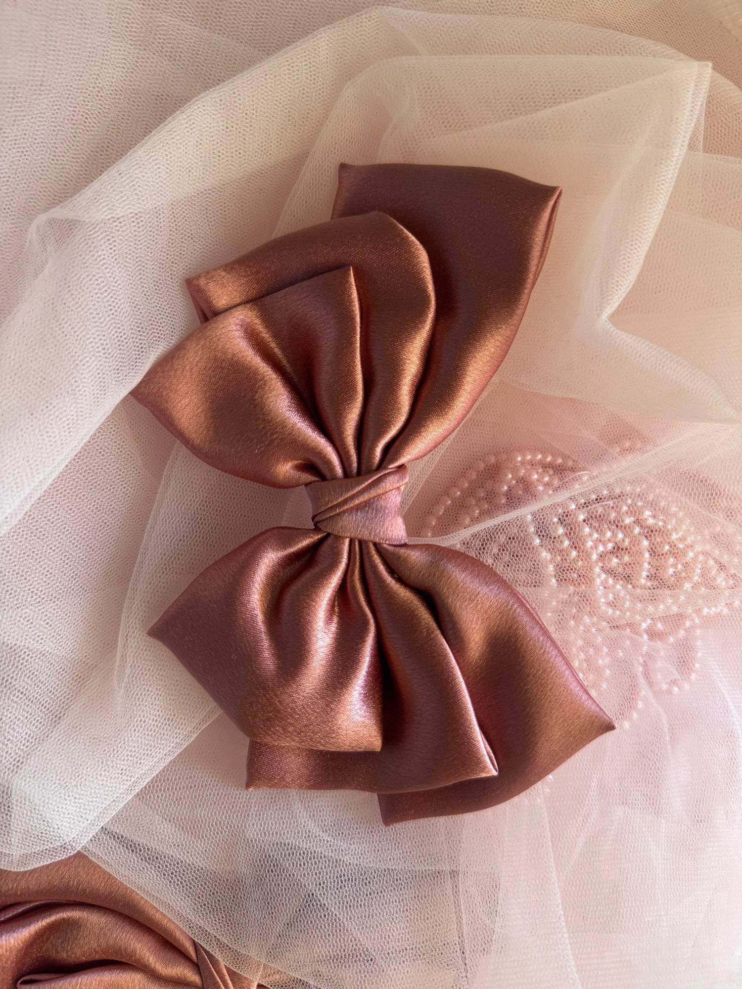 Metallic peach satin hair bow by Bows and Bags India displayed on blush tulle, showing luxurious fabric texture and elegant