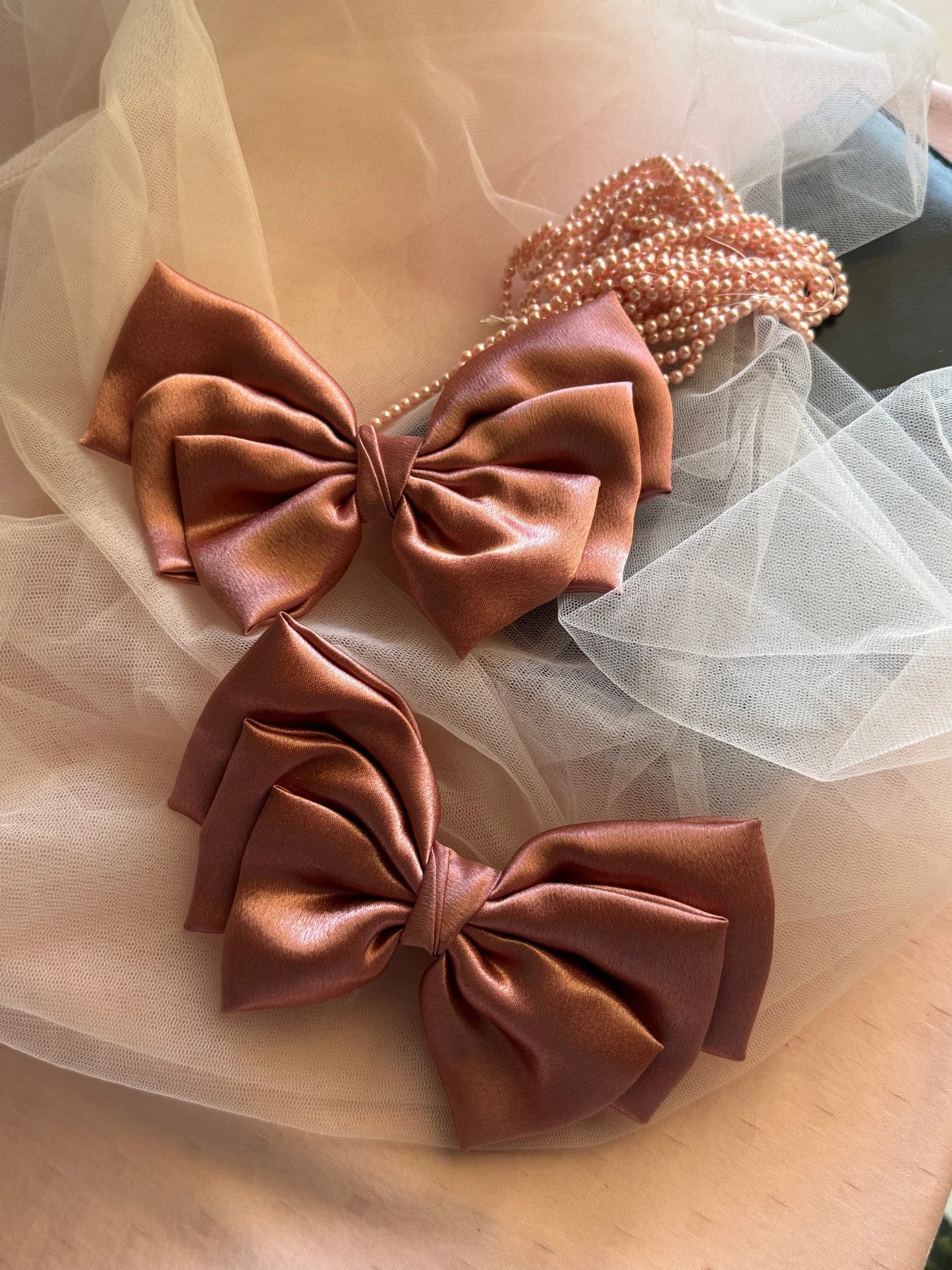 Metallic peach satin hair bows from Bows and Bags India displayed on tulle fabric with pearl beaded necklace, showing