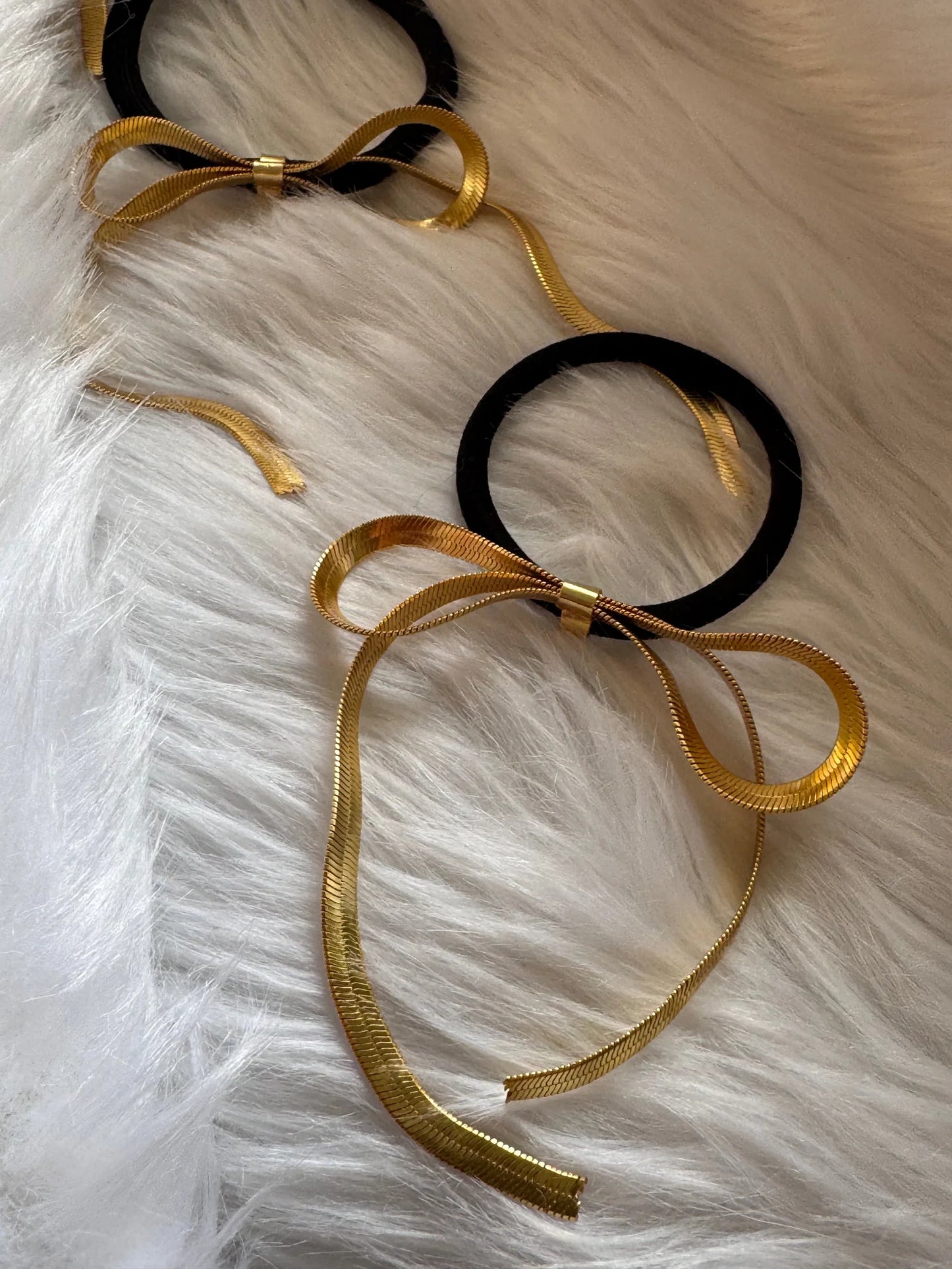 Golden chain bow metal rubber bands in black and gold displayed on white fur, handmade hair accessories by Bows and Bags