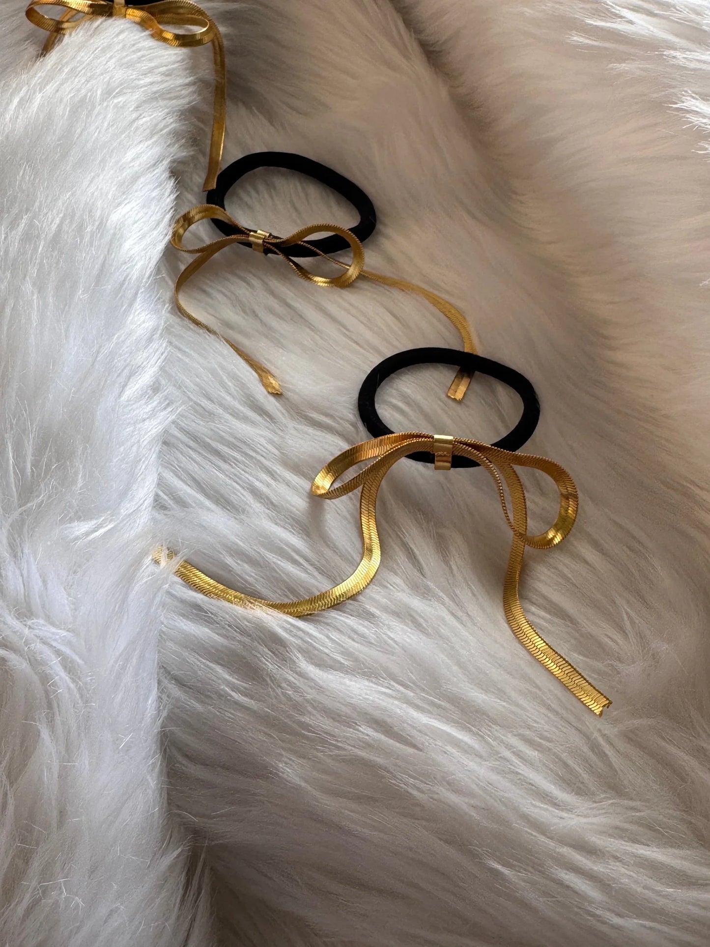 Golden Chain bow metal rubber bands in gold and black displayed on white fur, handmade hair accessories by Bows and Bags