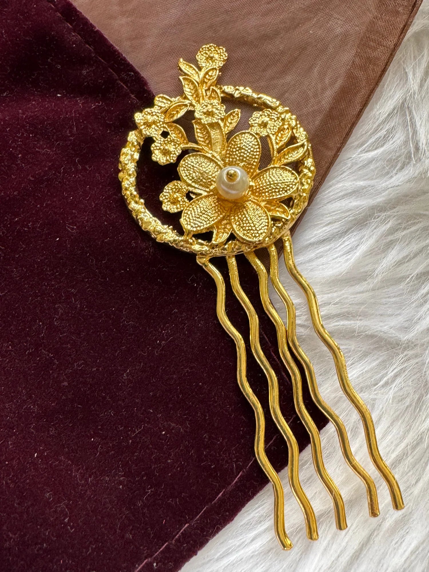 Golden Flora handmade hair pin with textured gold flowers and pearl center by Bows and Bags India, displayed on burgundy