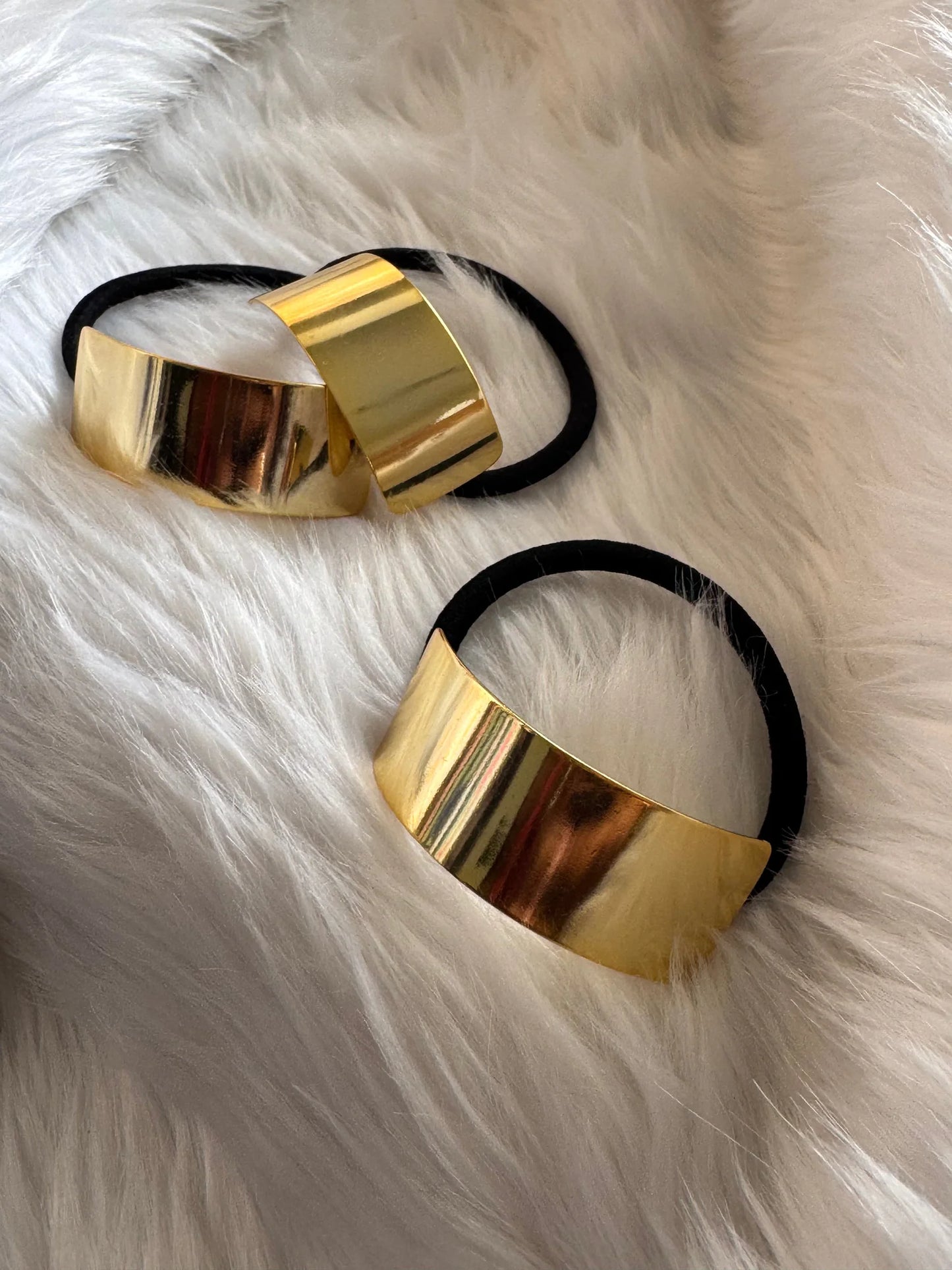Golden metal bar hair tie with geometric cuff design by Bows and Bags India, flat lay on white fur showing reflective gold