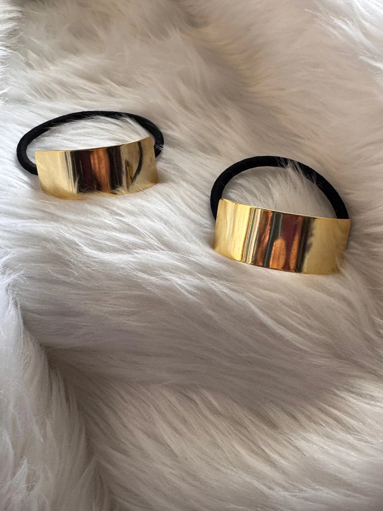 Two golden metal bar hair ties with black elastic bands on white fur, showcasing metallic cuff design by Bows and Bags India