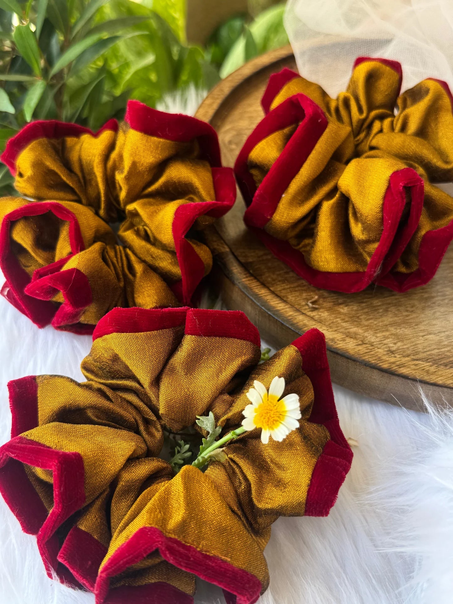 Golden yellow and maroon velvet silk scrunchies by Bows and Bags India displayed on wooden plate with daisy flower detail
