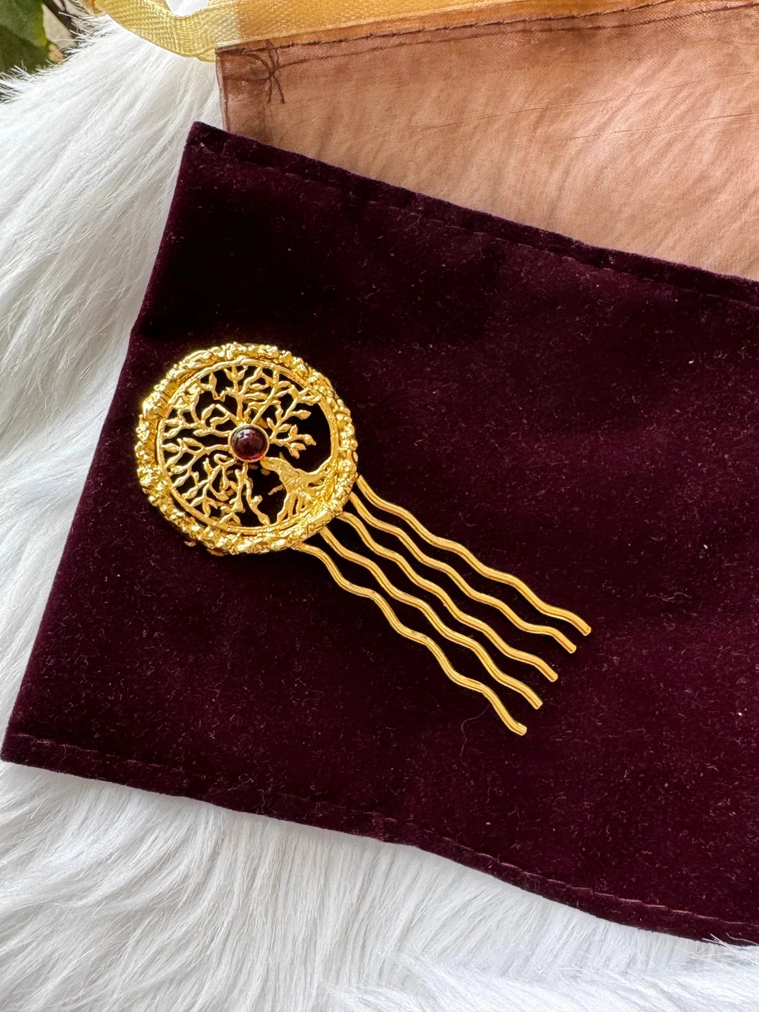 Golden Tree hair pin with intricate tree of life design, deep red stone center, and wavy gold prongs on burgundy velvet by