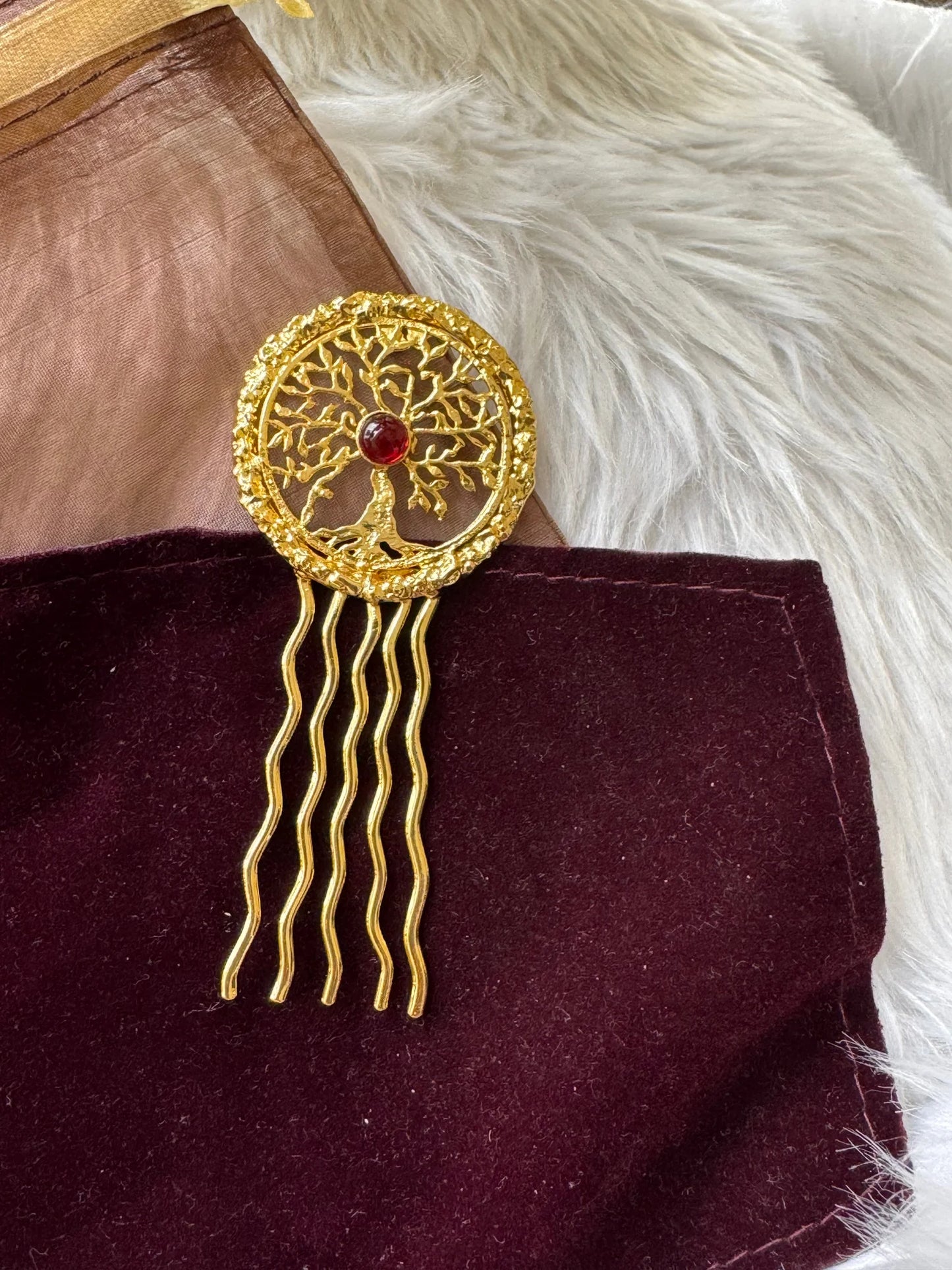 Golden Tree hair pin with intricate tree of life design, deep red stone center, and wavy gold prongs on burgundy velvet by