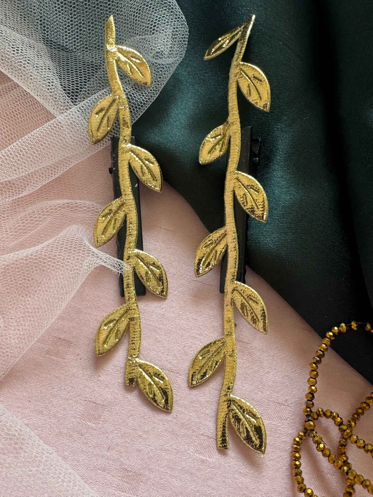 Golden Twig hair clips in brushed gold with leaf details displayed on dusty pink and forest green fabric by Bows and Bags