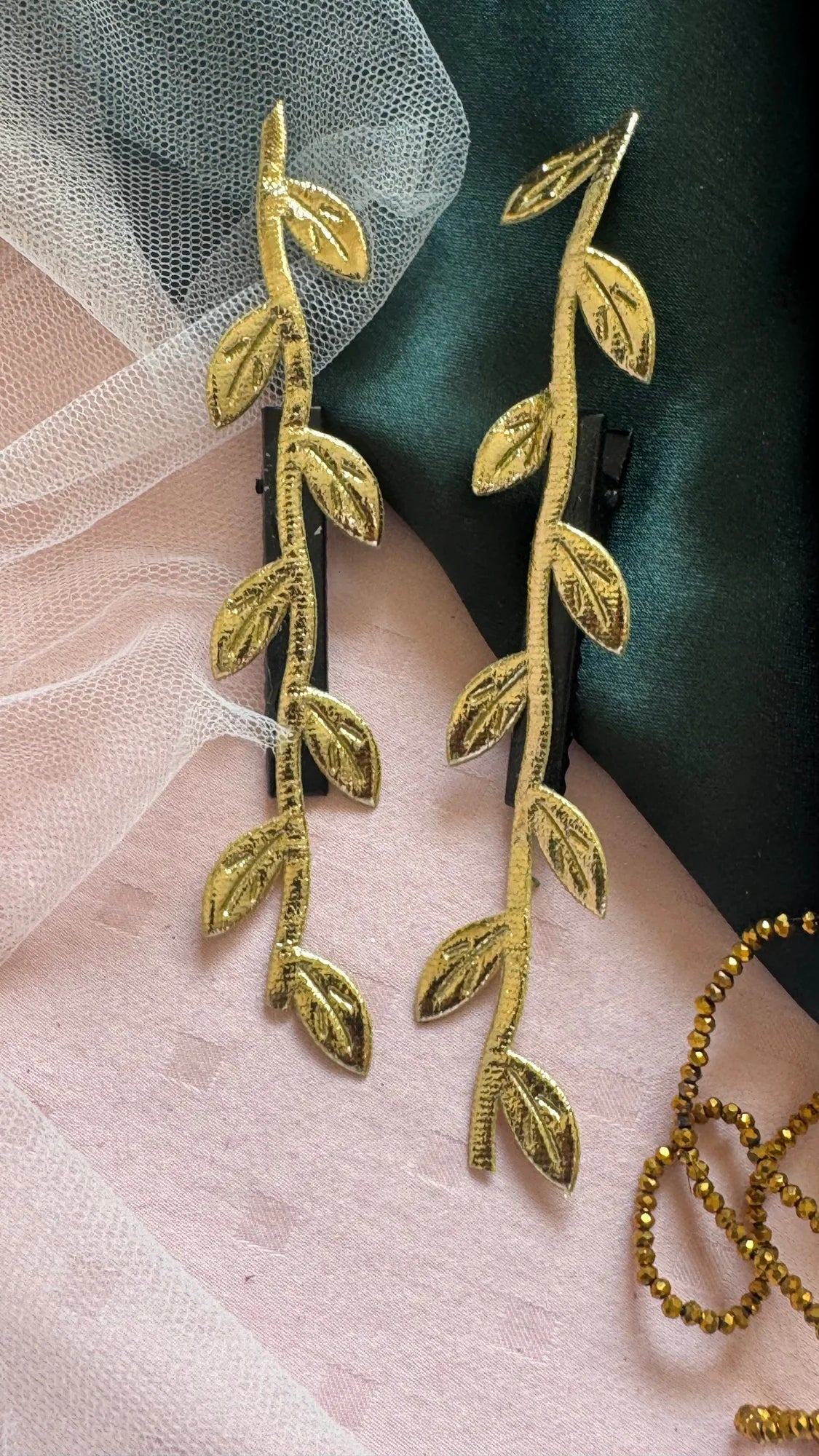 Golden Twig handmade hair clip pair in gold leaf design displayed on blush and forest green fabric by Bows and Bags India
