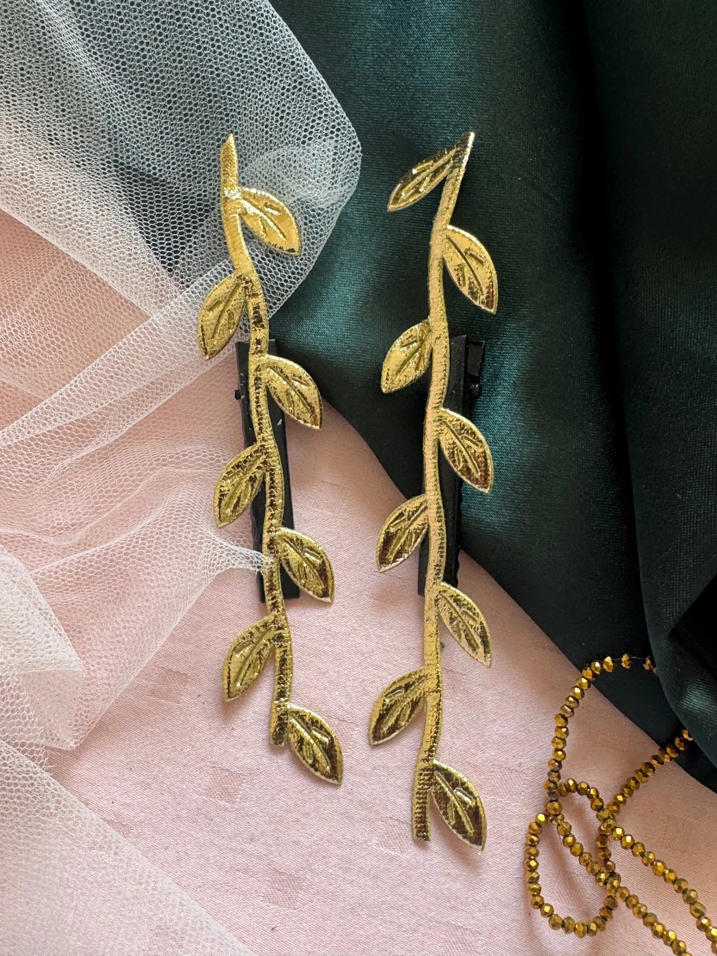 Golden Twig hair clip pair by Bows and Bags India with delicate gold leaf details on pink and green fabric backdrop