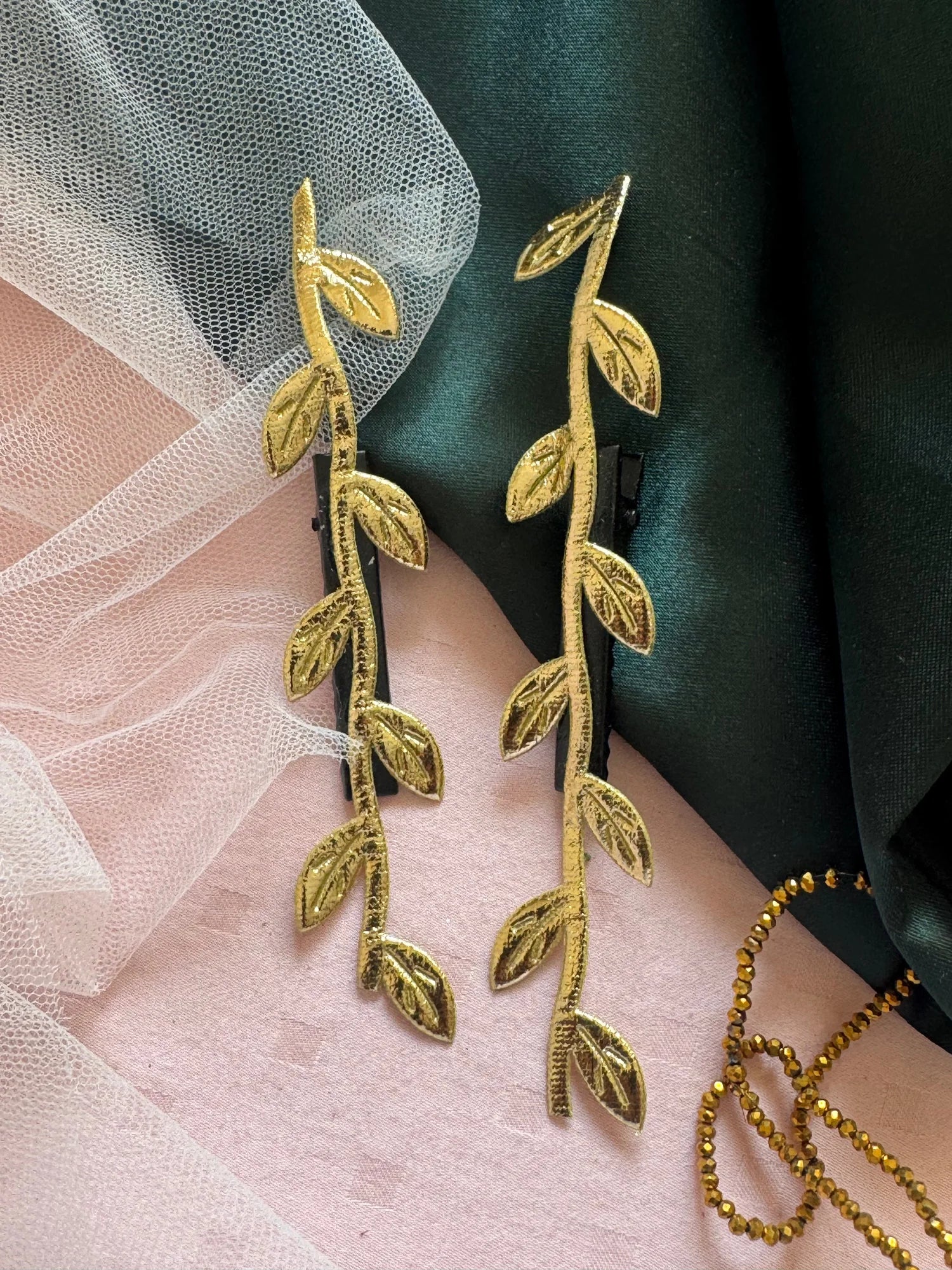 Golden Twig hair clip pair by Bows and Bags India with delicate gold leaf details on pink and green fabric backdrop