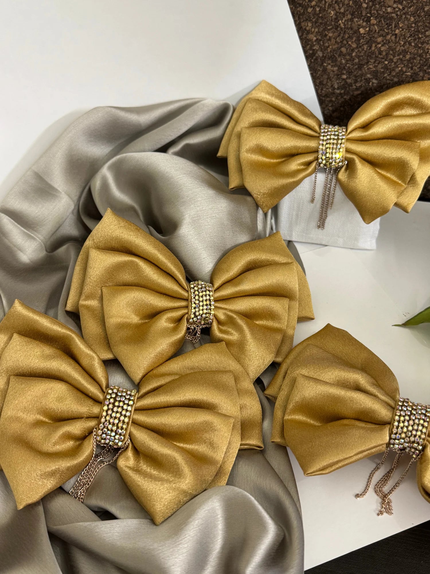 Goldy Bling golden satin hair bow with stone and chain detailing, displayed with silver fabric by Bows and Bags India