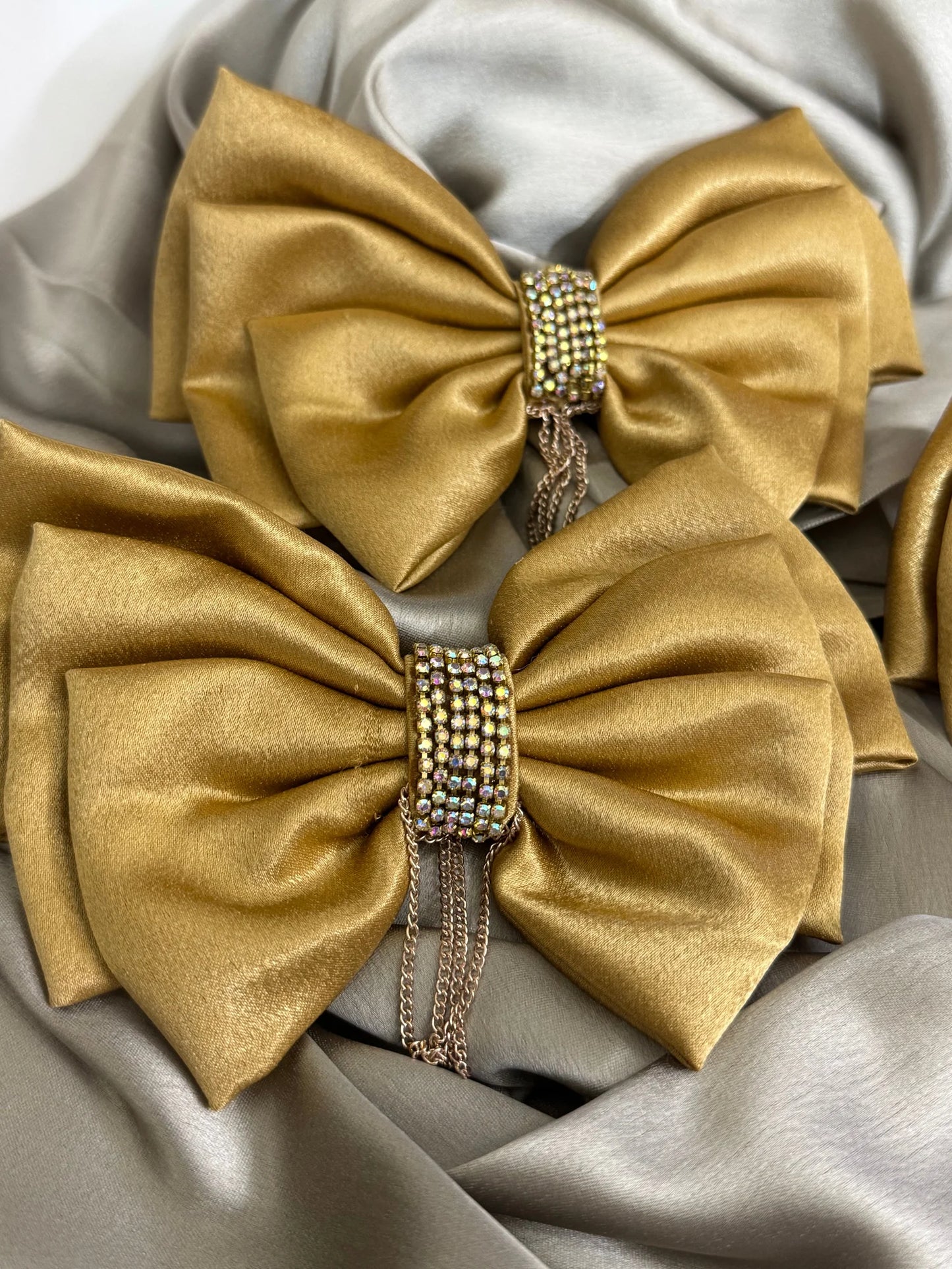 Gold satin hair bows with stone and chain embellishments by Bows and Bags India, handmade accessory detail shot on neutral