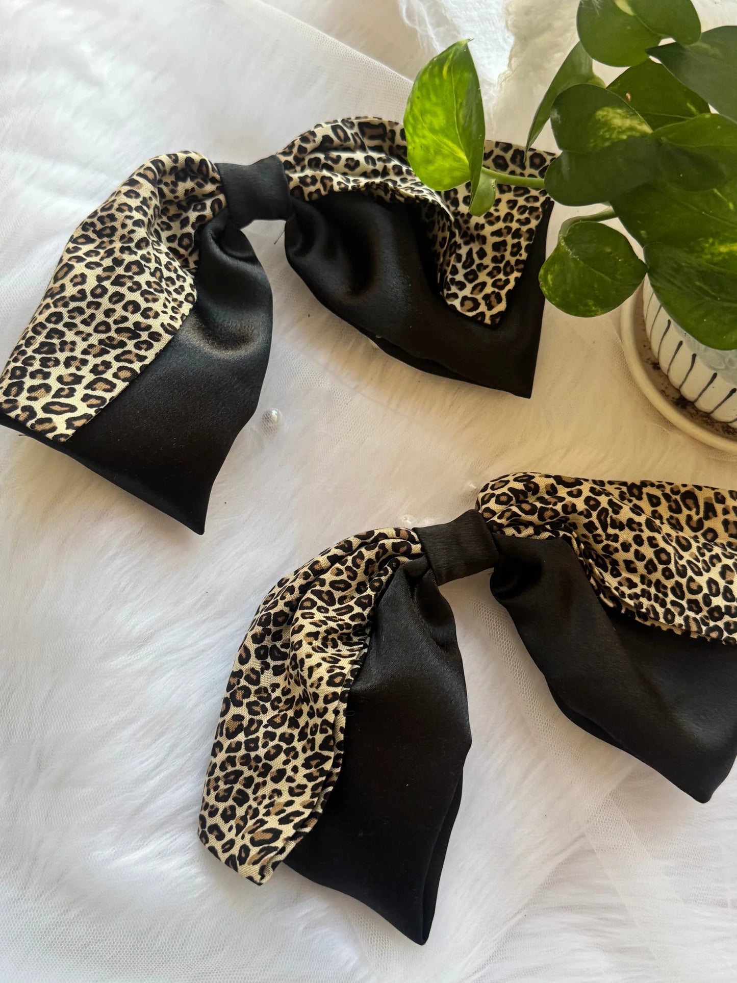 Black satin and leopard print handmade hair bows by Bows and Bags India displayed on white surface with green plant styling