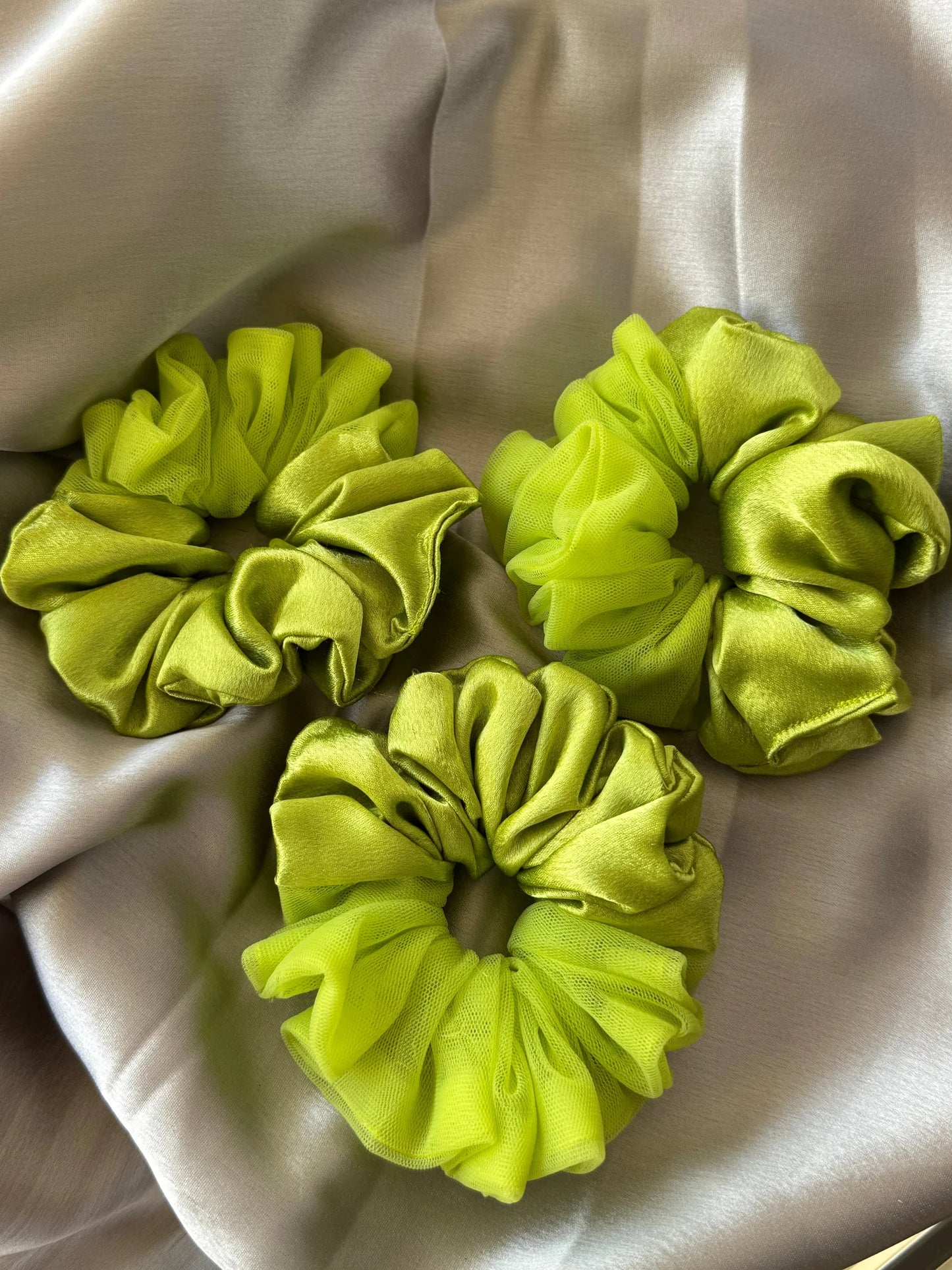 Three neon green satin scrunchies with delicate net borders by Bows and Bags India displayed on cream fabric, showing