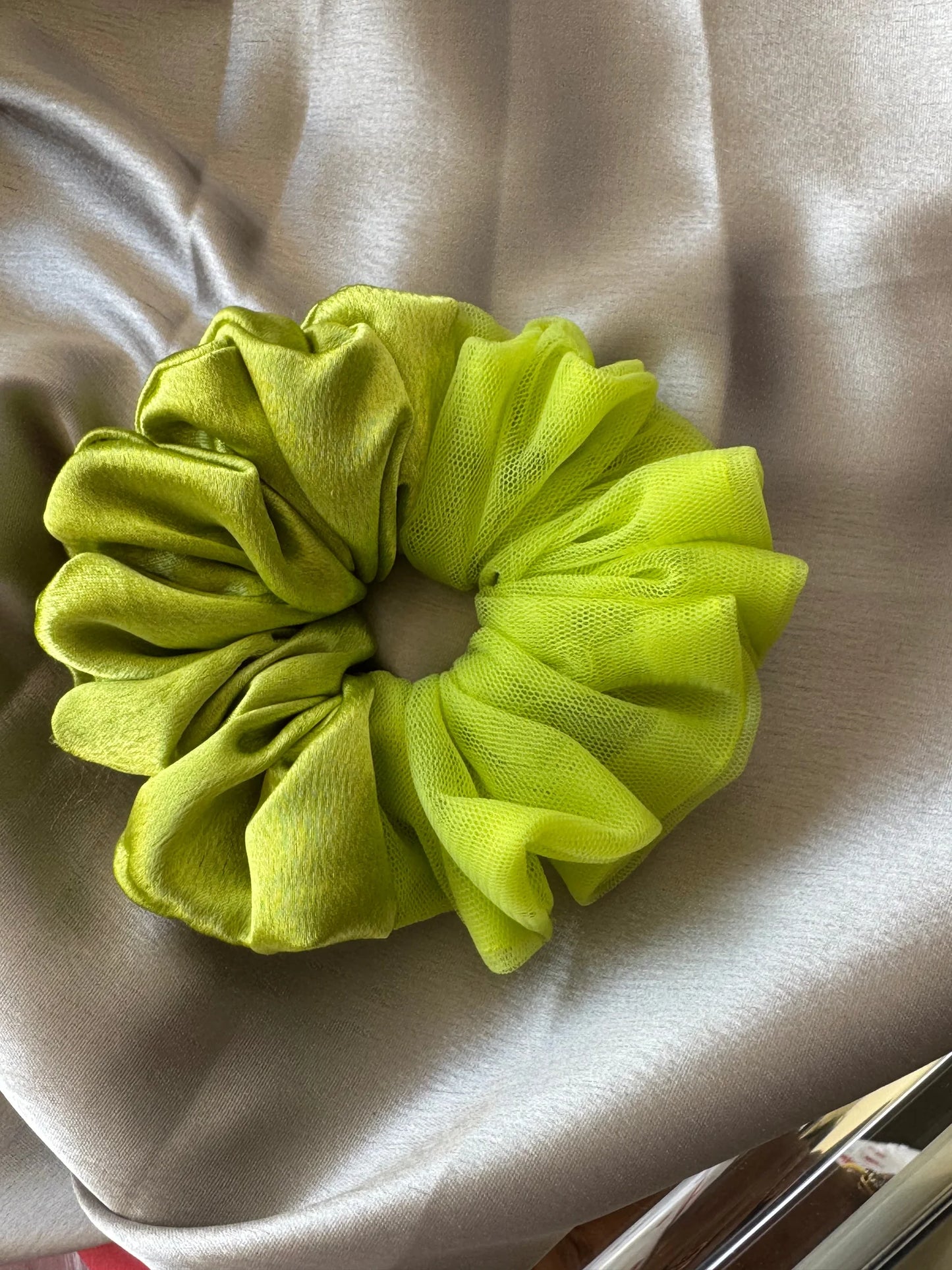 Neon green satin and net scrunchie with ruffled texture displayed on beige fabric by Bows and Bags India