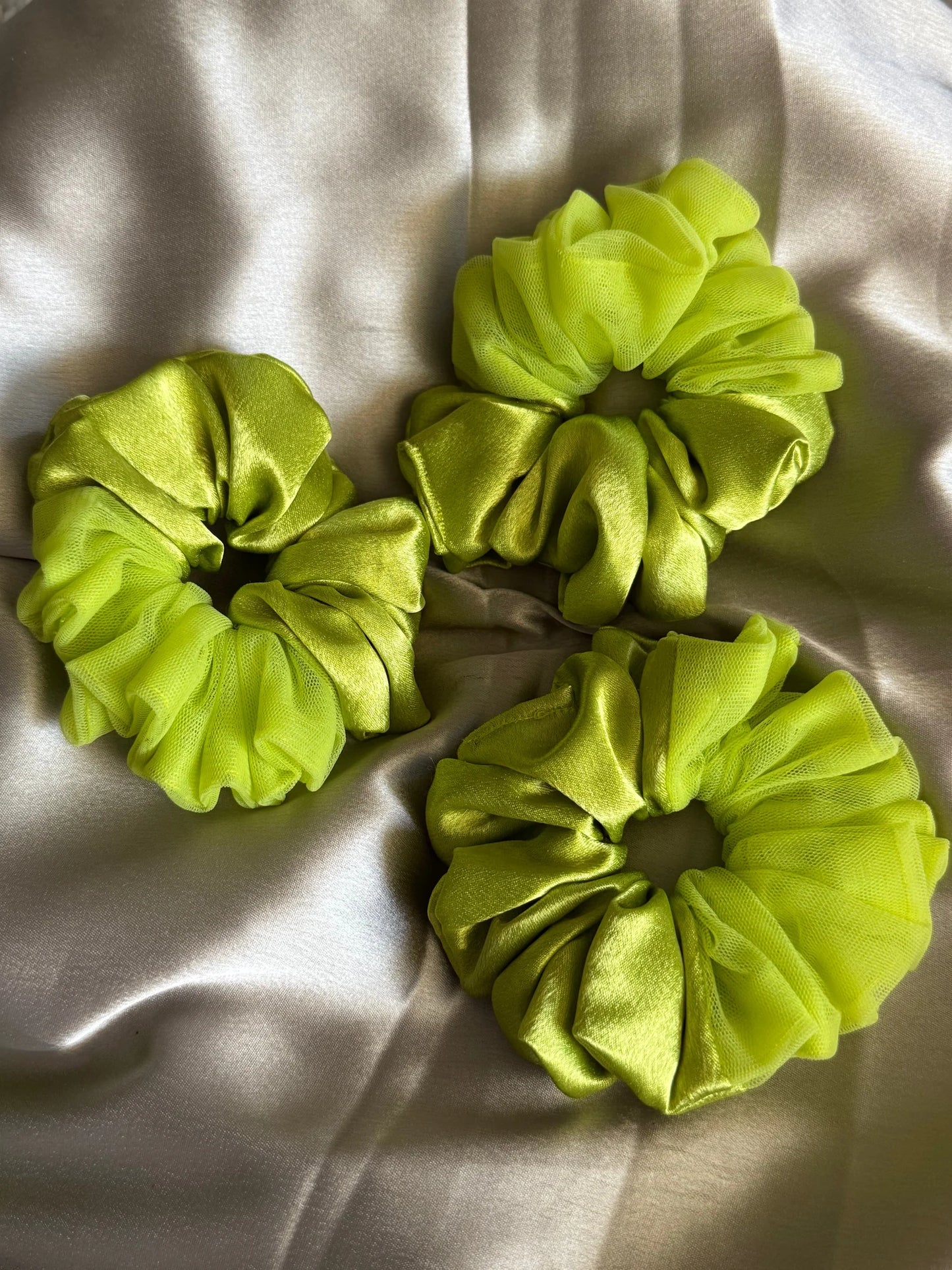 Three neon green satin and net scrunchies by Bows and Bags India displayed on cream fabric, showing textured detail and