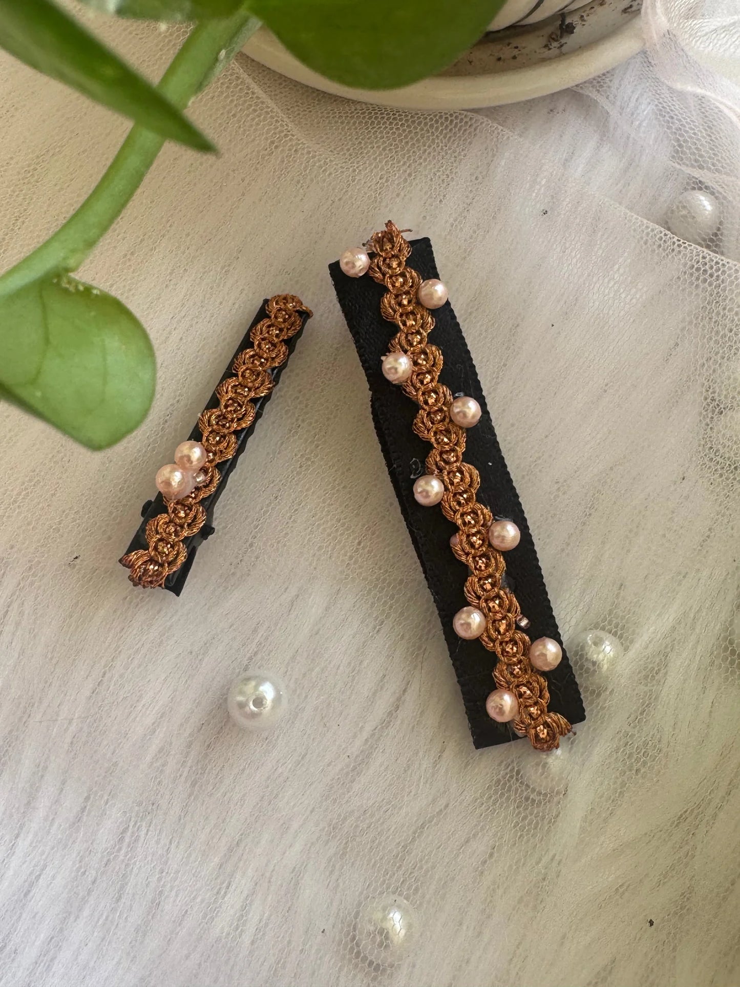 Two handmade pearl embroidered hair clips by Bows and Bags India with golden crochet detail on black fabric, displayed on