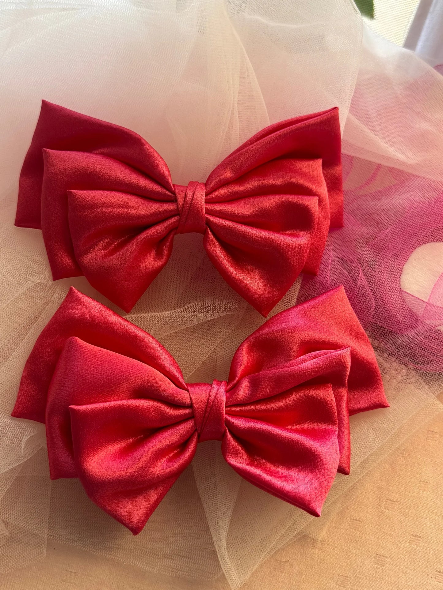 Two hot pink satin hair bows by Bows and Bags India displayed on tulle fabric, showing handmade craftsmanship and glossy